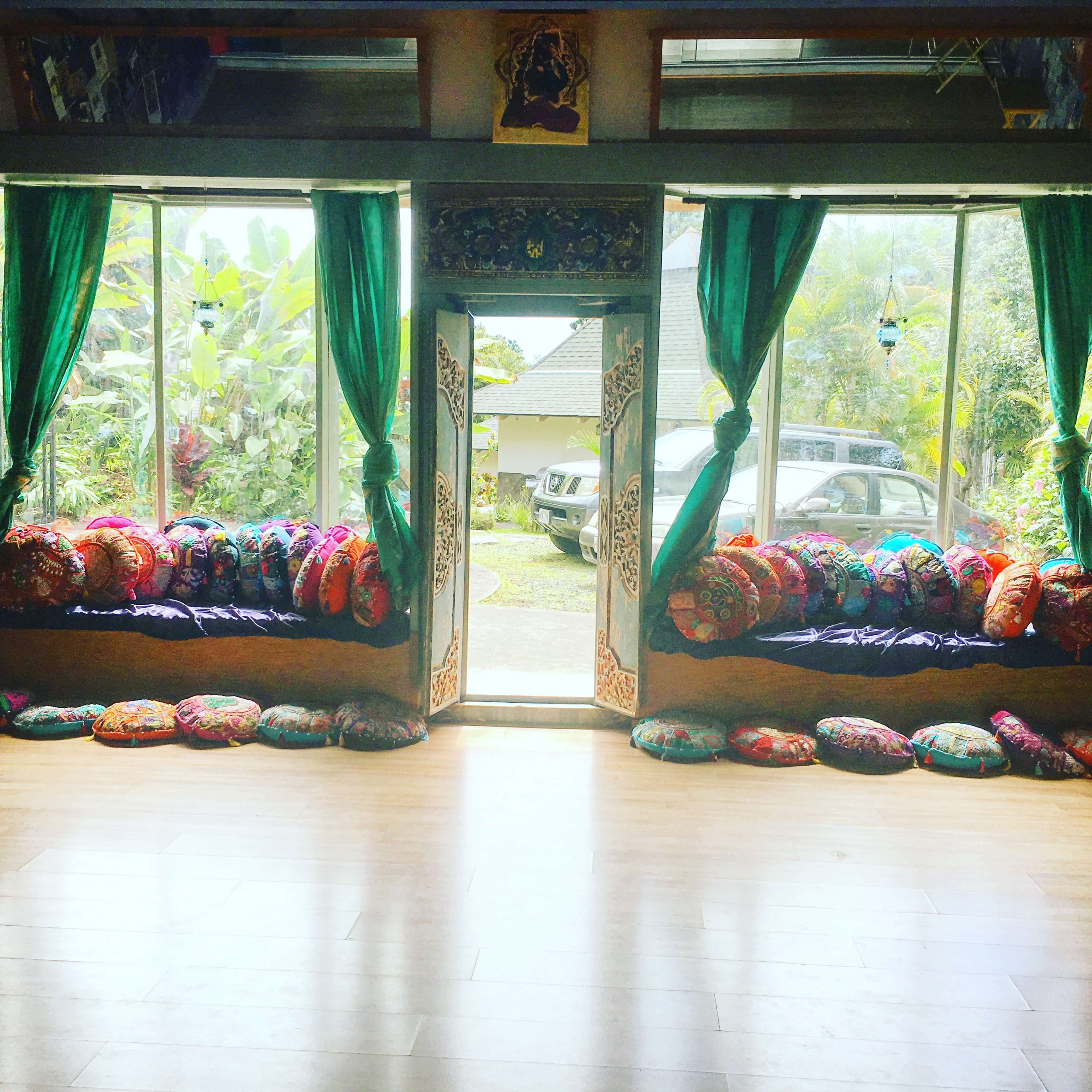 A room with vibrant cushions arranged along the walls and large open doors leading to a view of greenery outside.