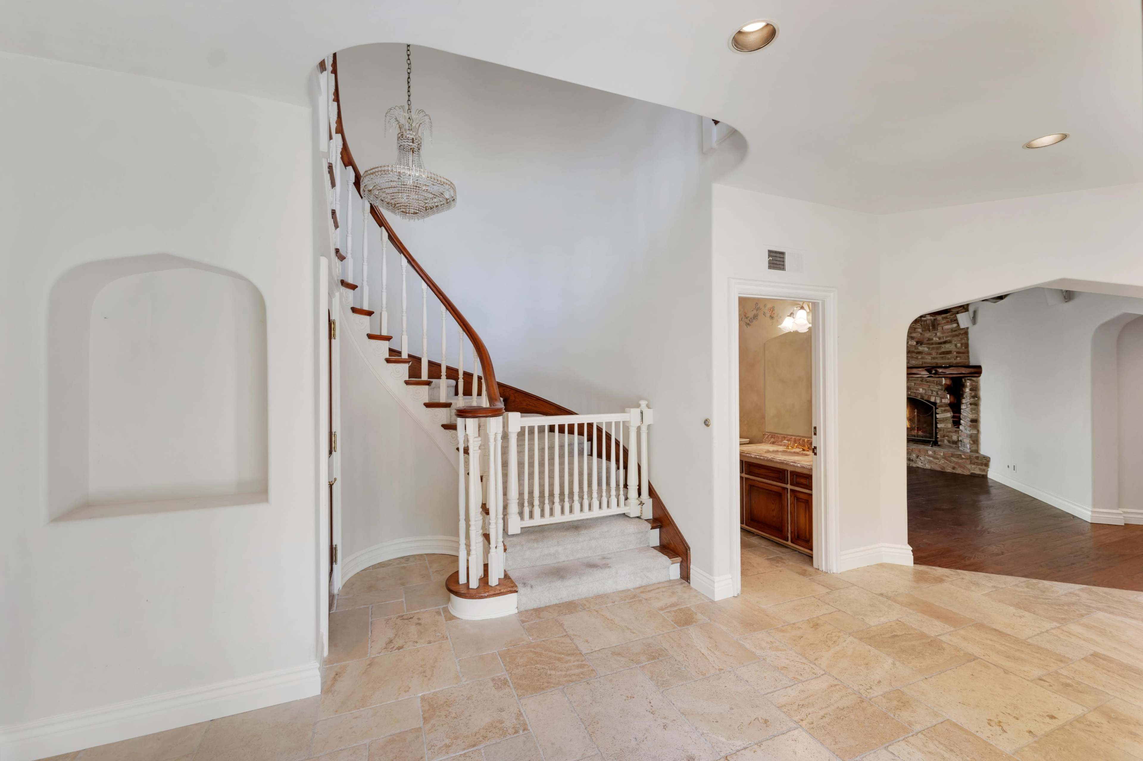A staircase with a wooden handrail is positioned against a light-colored wall in a spacious entryway, leading to the upper floor of a house.