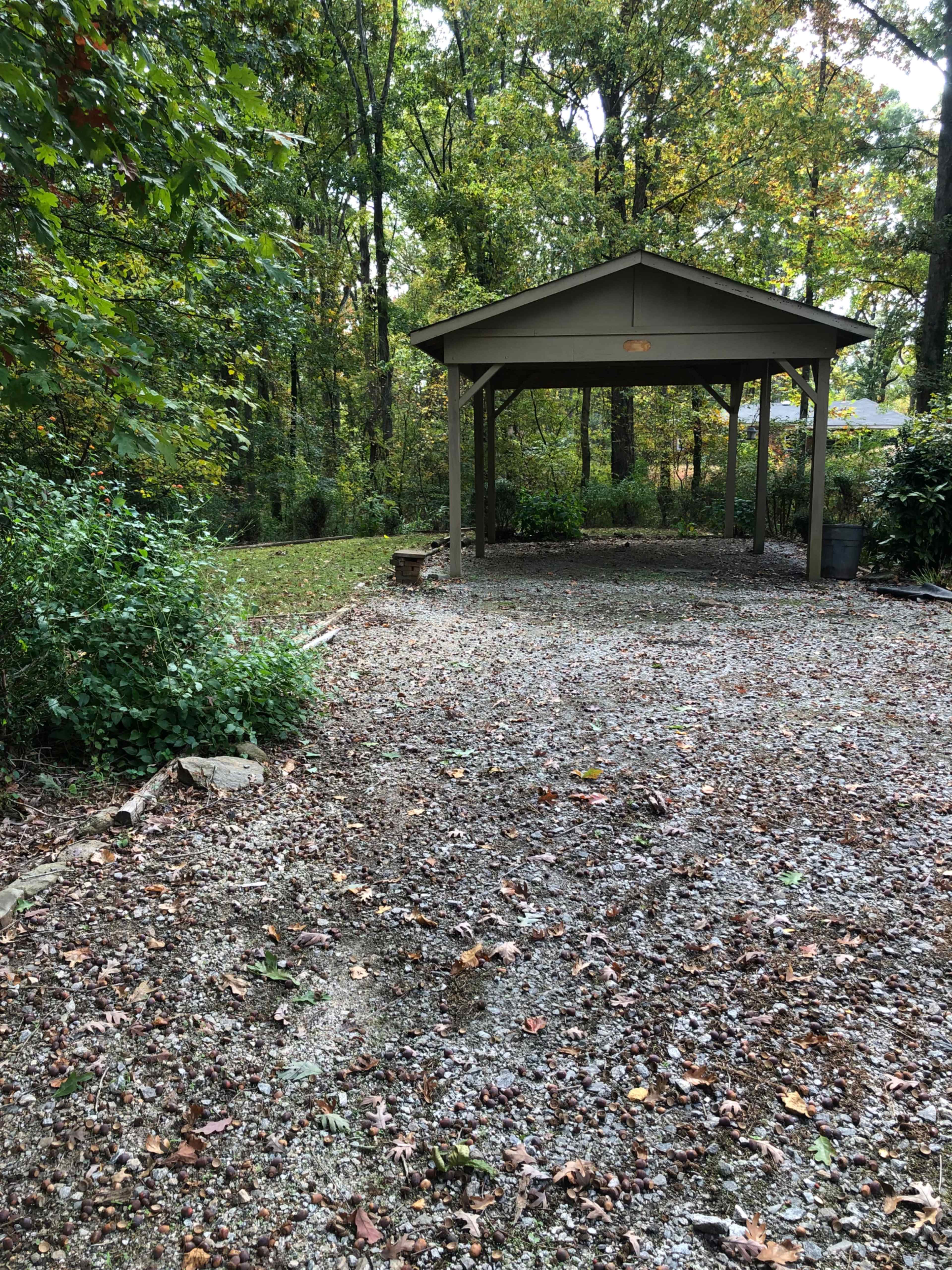 A gravel area with a covered structure is surrounded by trees and foliage.