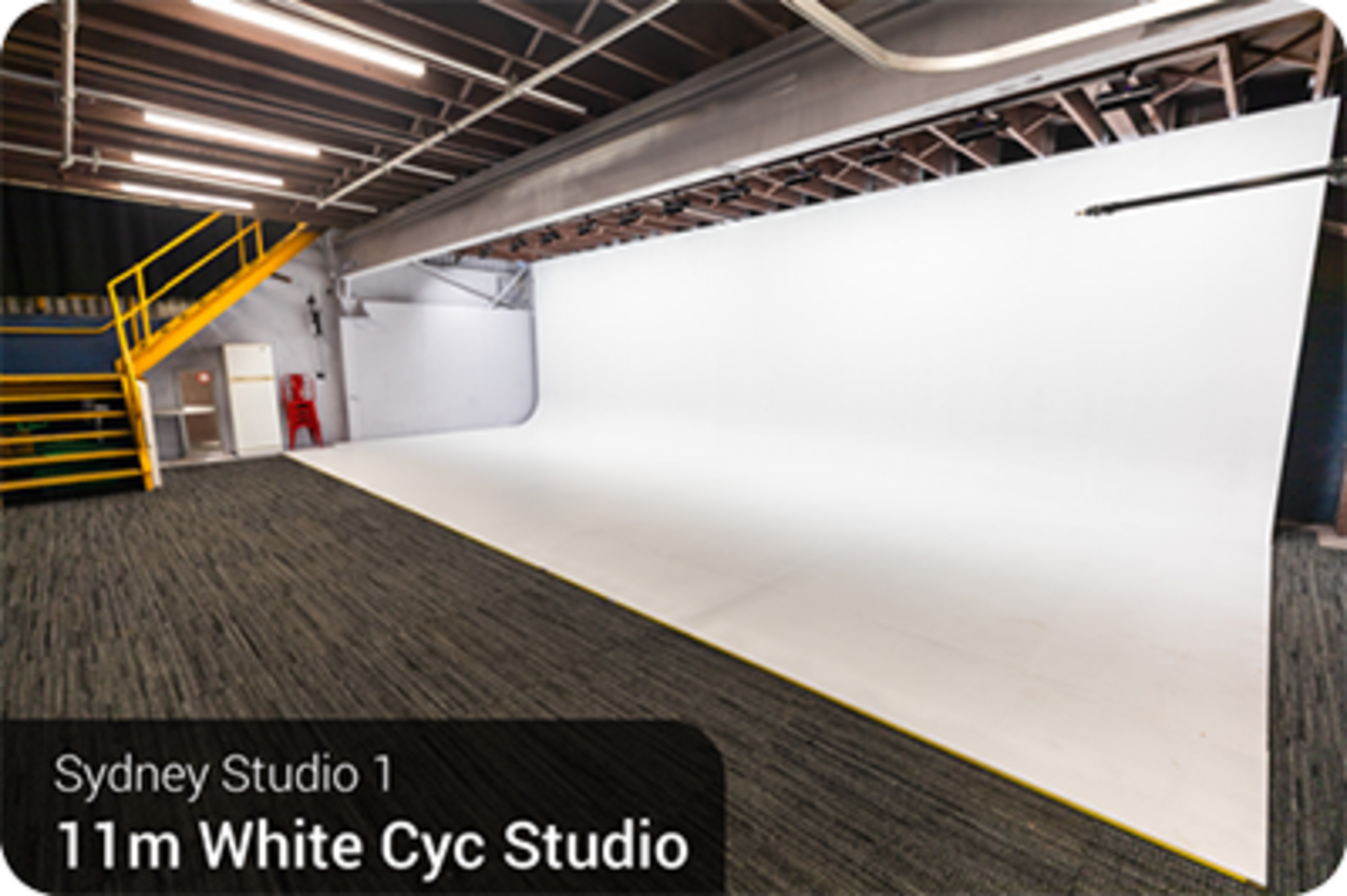 The image shows a large white cyc studio with a seamless backdrop and a staircase leading to an upper level.