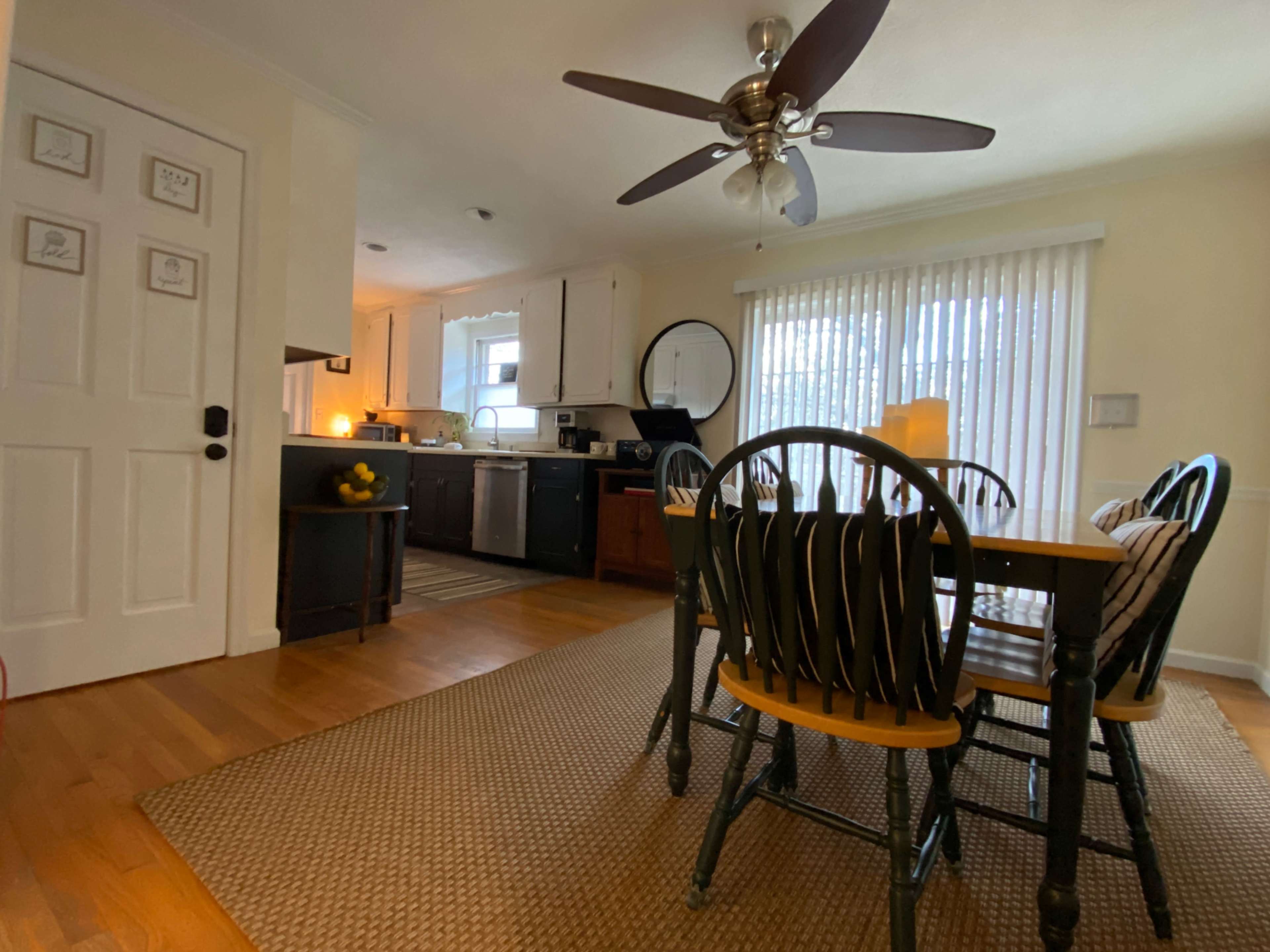 A dining area with a wooden table and six chairs, adjacent to a kitchen featuring light-colored cabinets and kitchen appliances.