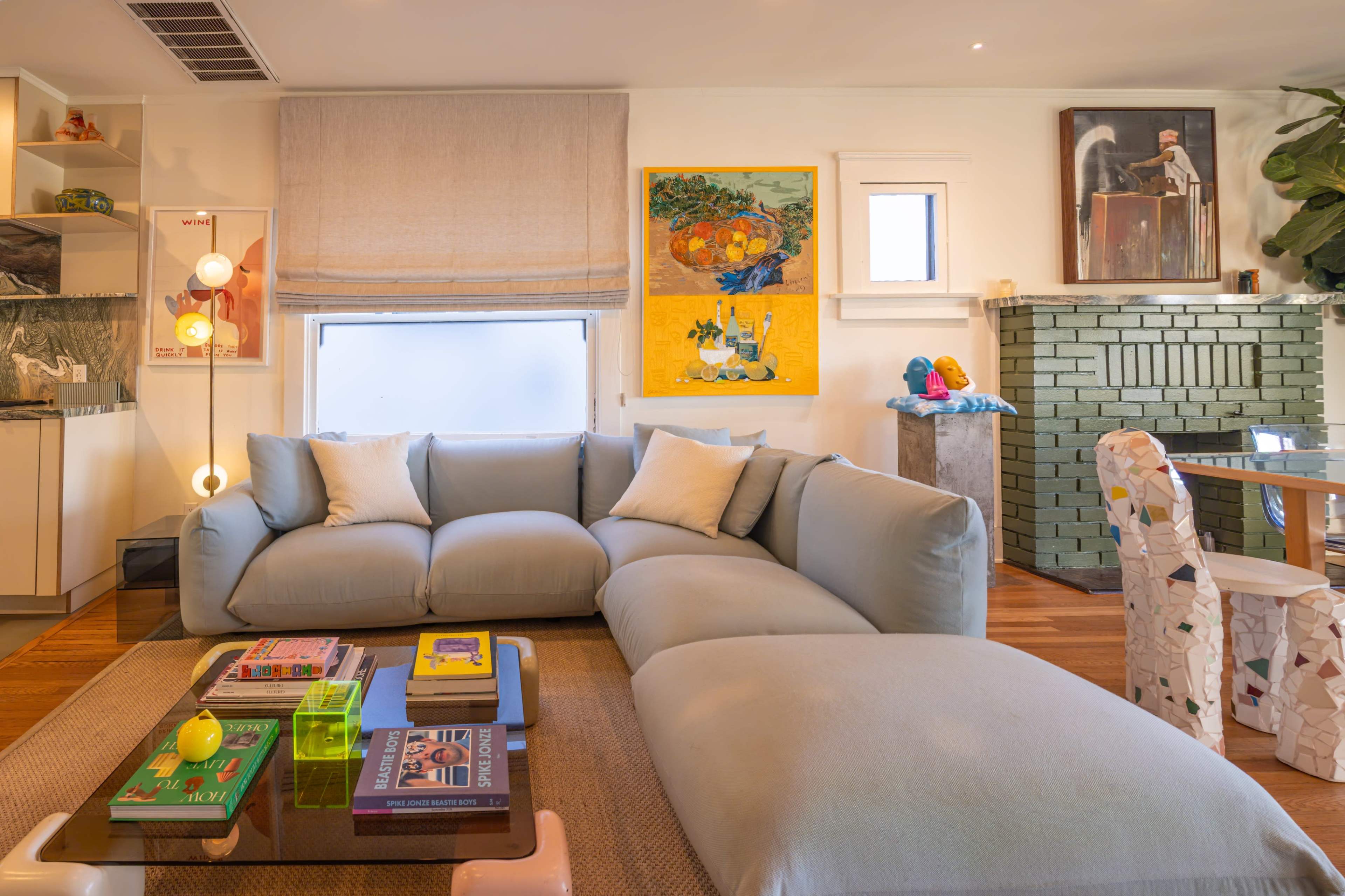 The living room features a light blue sectional sofa, a coffee table with books and decorative items, and colorful artwork on the walls.