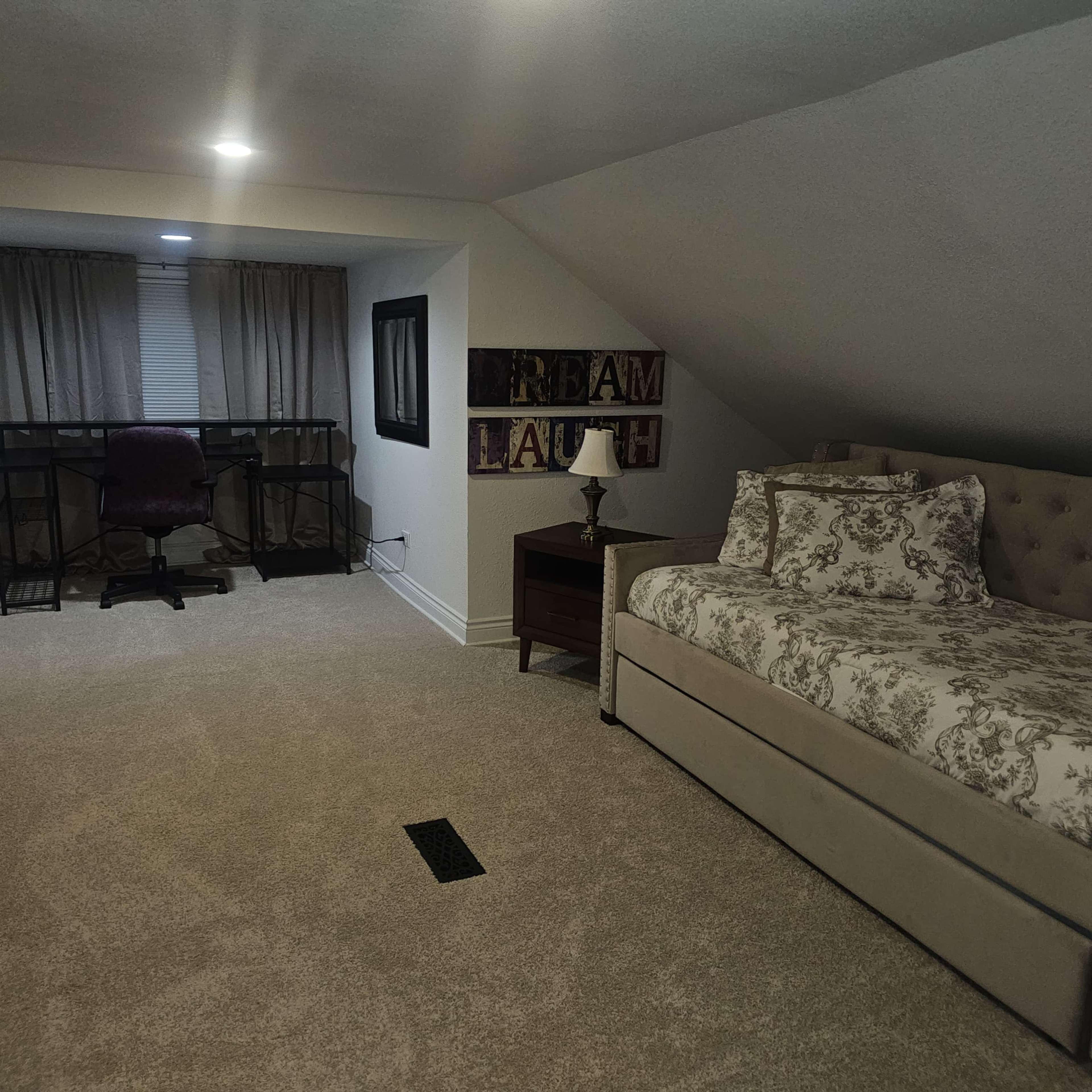 The image shows a cozy attic space featuring a bed, a desk with a chair, and a side table.