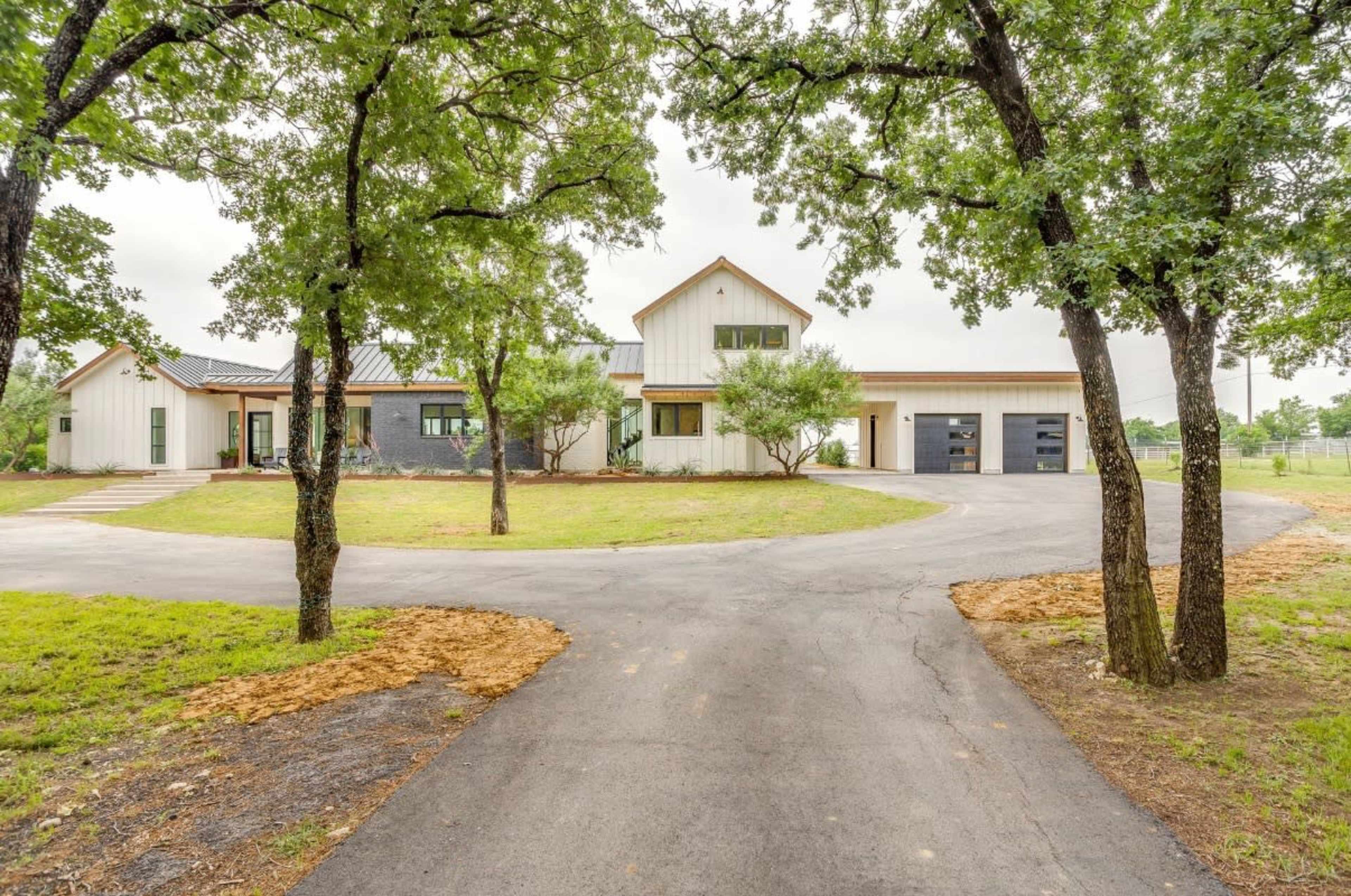 A contemporary house with a mixed exterior design is seen surrounded by trees and a circular driveway.