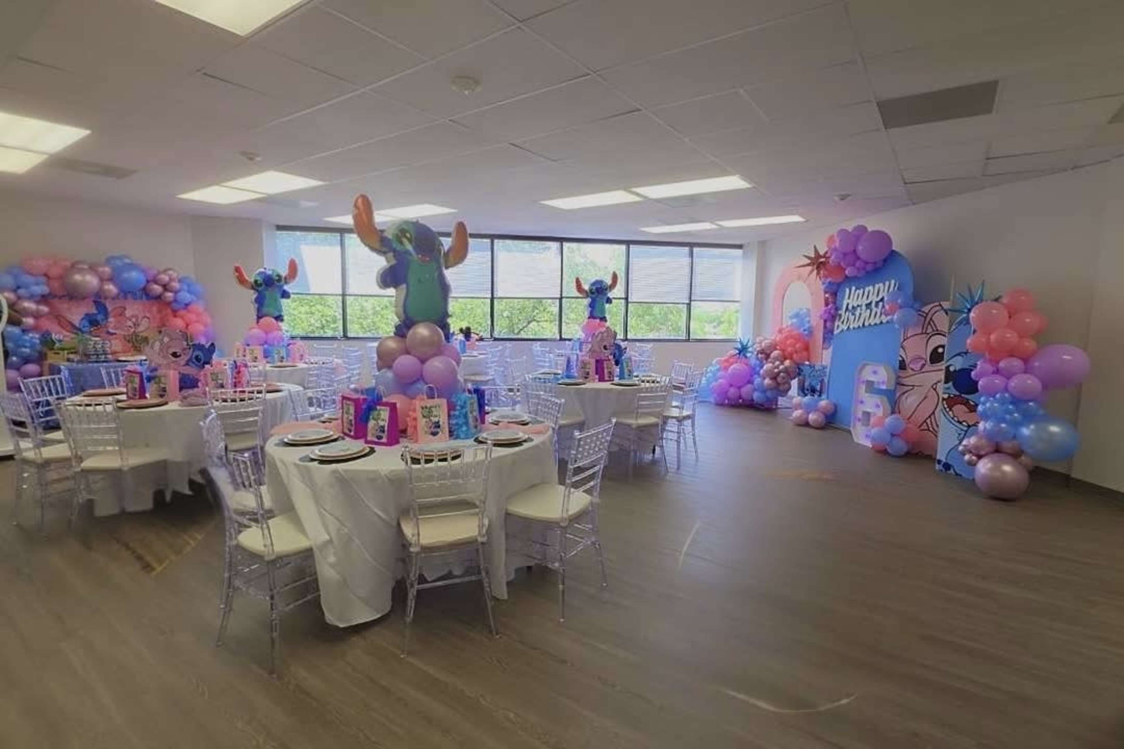 The image shows a decorated party room with tables set for a celebration, featuring colorful balloons and themed decorations.