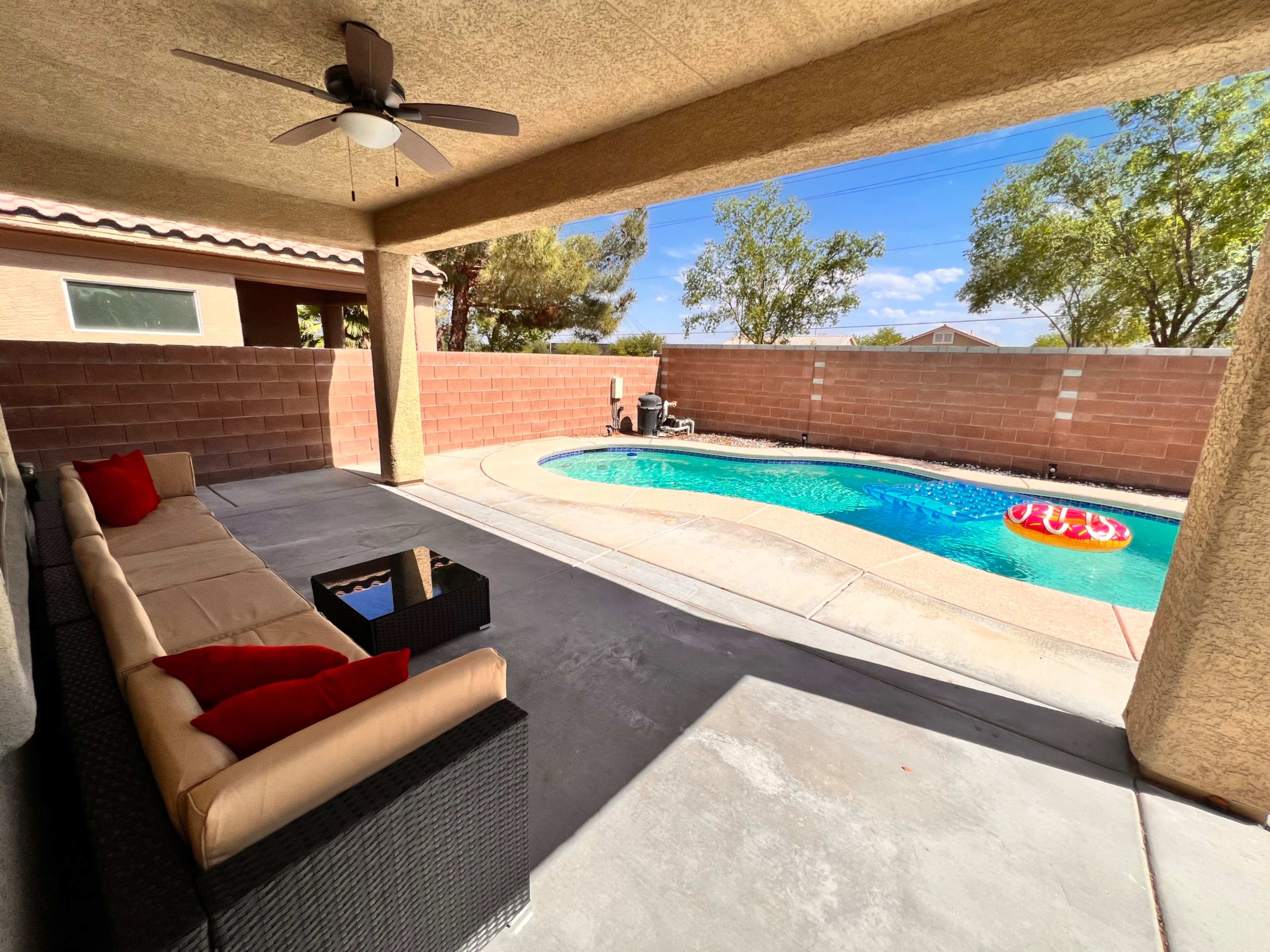 A covered patio features a seating area and overlooks a swimming pool enclosed by a brick wall.