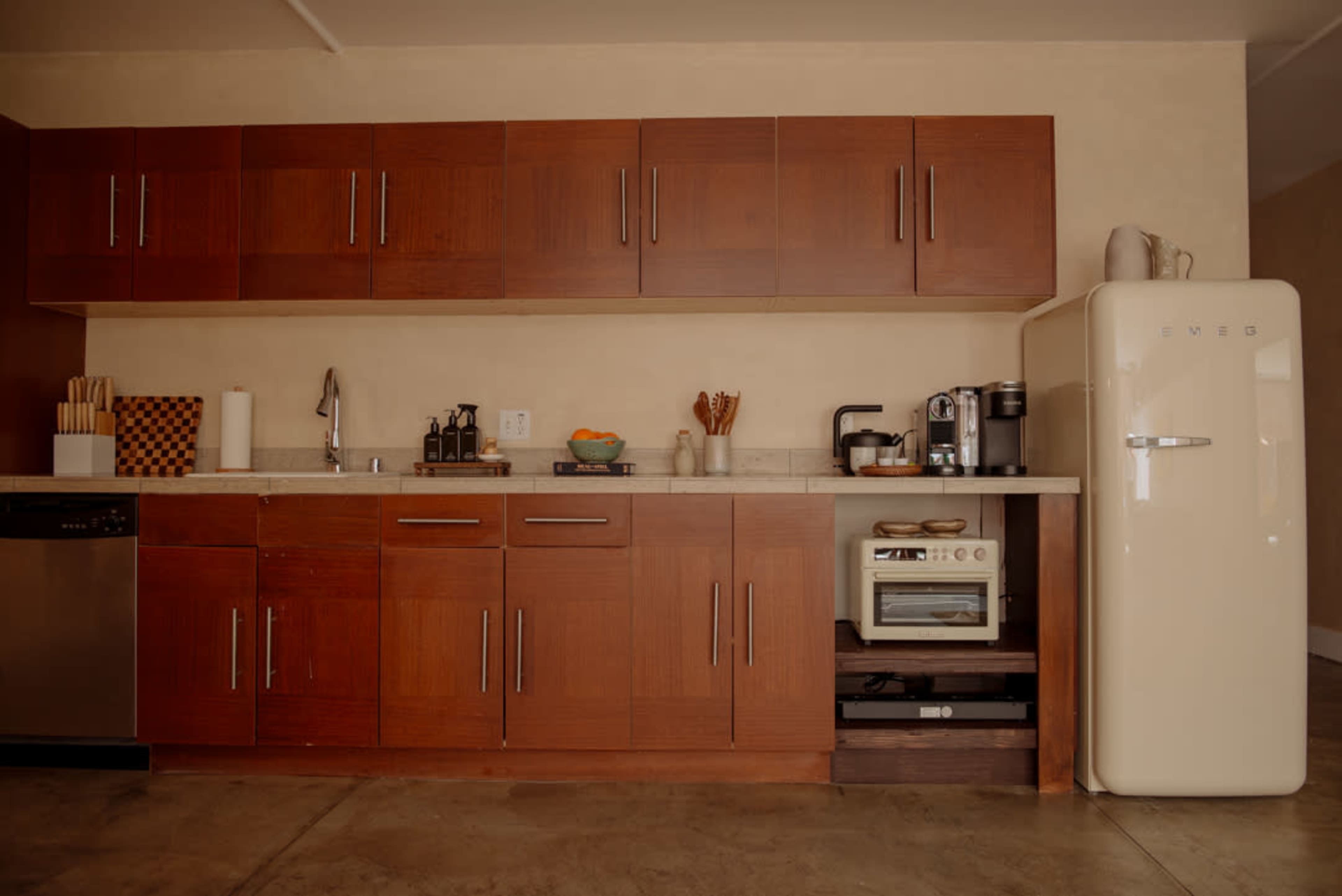 The image shows a modern kitchen with wooden cabinets, a stainless steel dishwasher, a black countertop, and a vintage-style refrigerator.