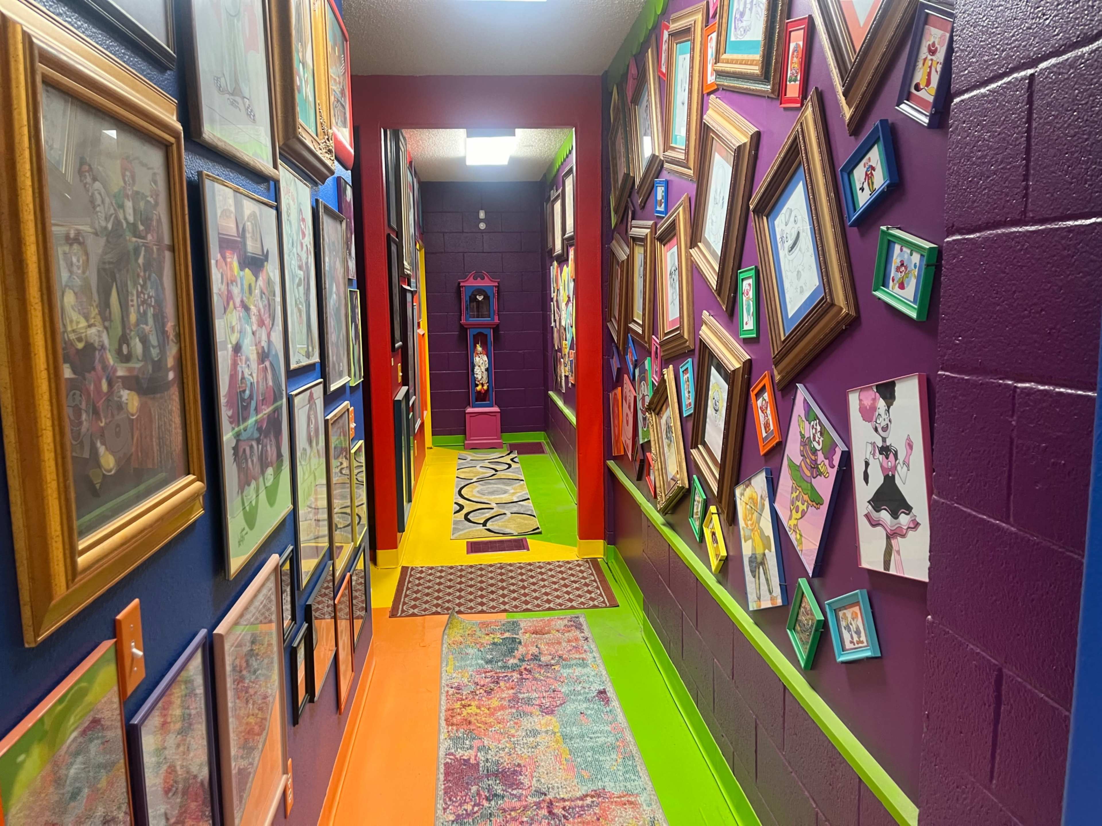 The image shows a colorful hallway adorned with framed artwork and photographs on both sides, leading to an archway at the end.