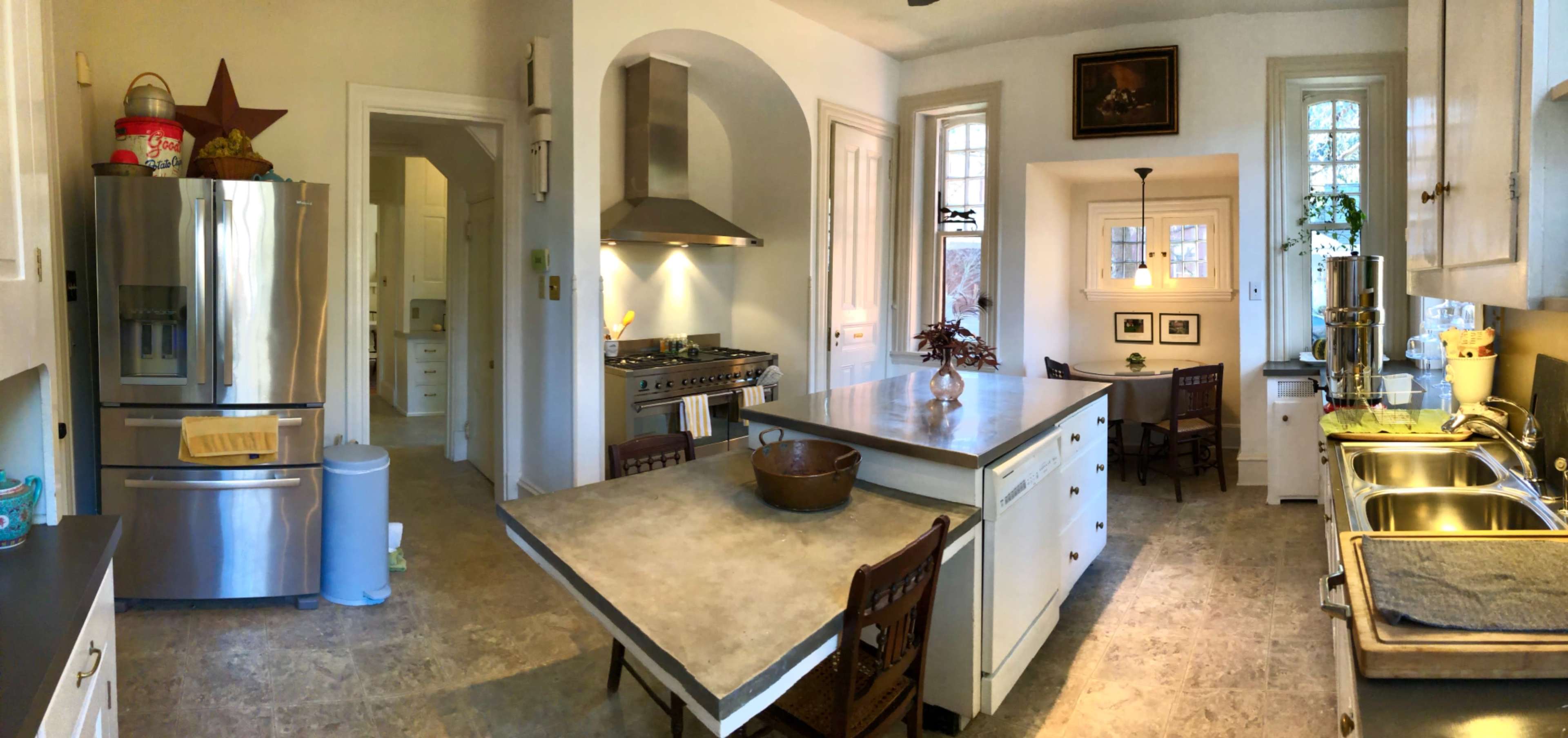 A spacious kitchen featuring stainless steel appliances, including a large refrigerator and a gas stove, with an island and adjacent dining area.