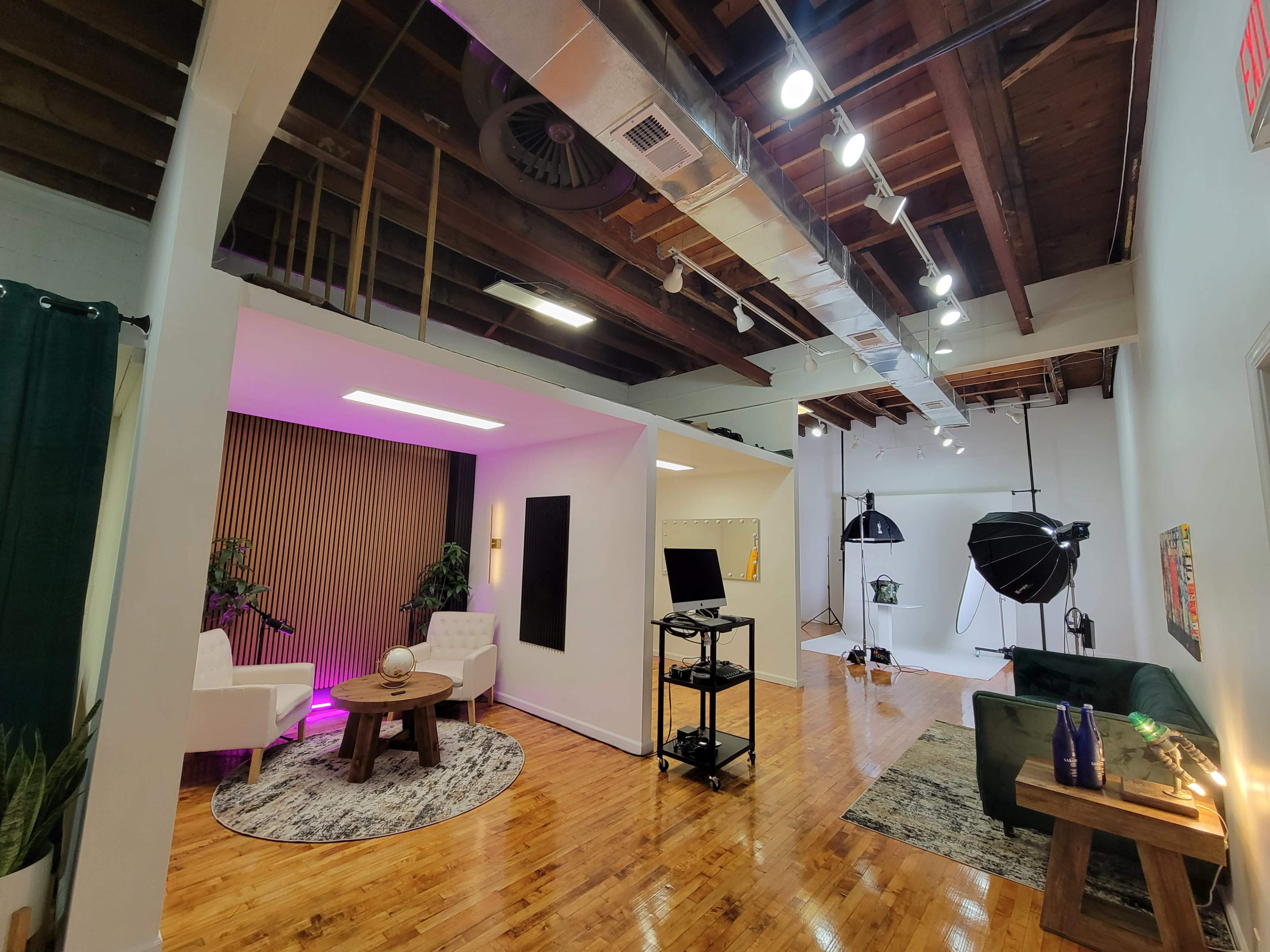 The image shows a modern interior space with seating areas, a green couch, lighting equipment, and a polished wooden floor.