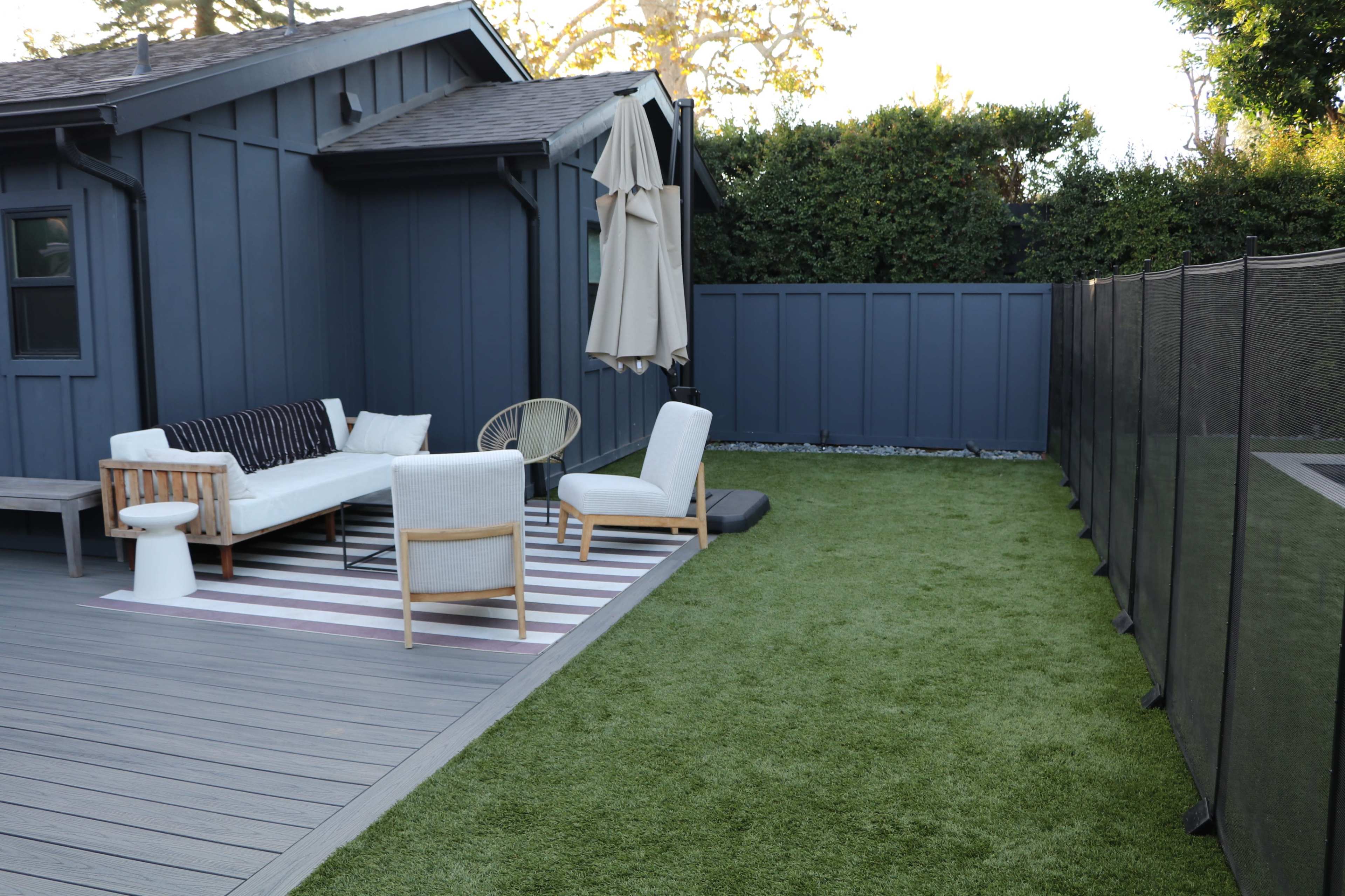 A patio area with a furniture set, an umbrella, and artificial grass surrounded by a fence.