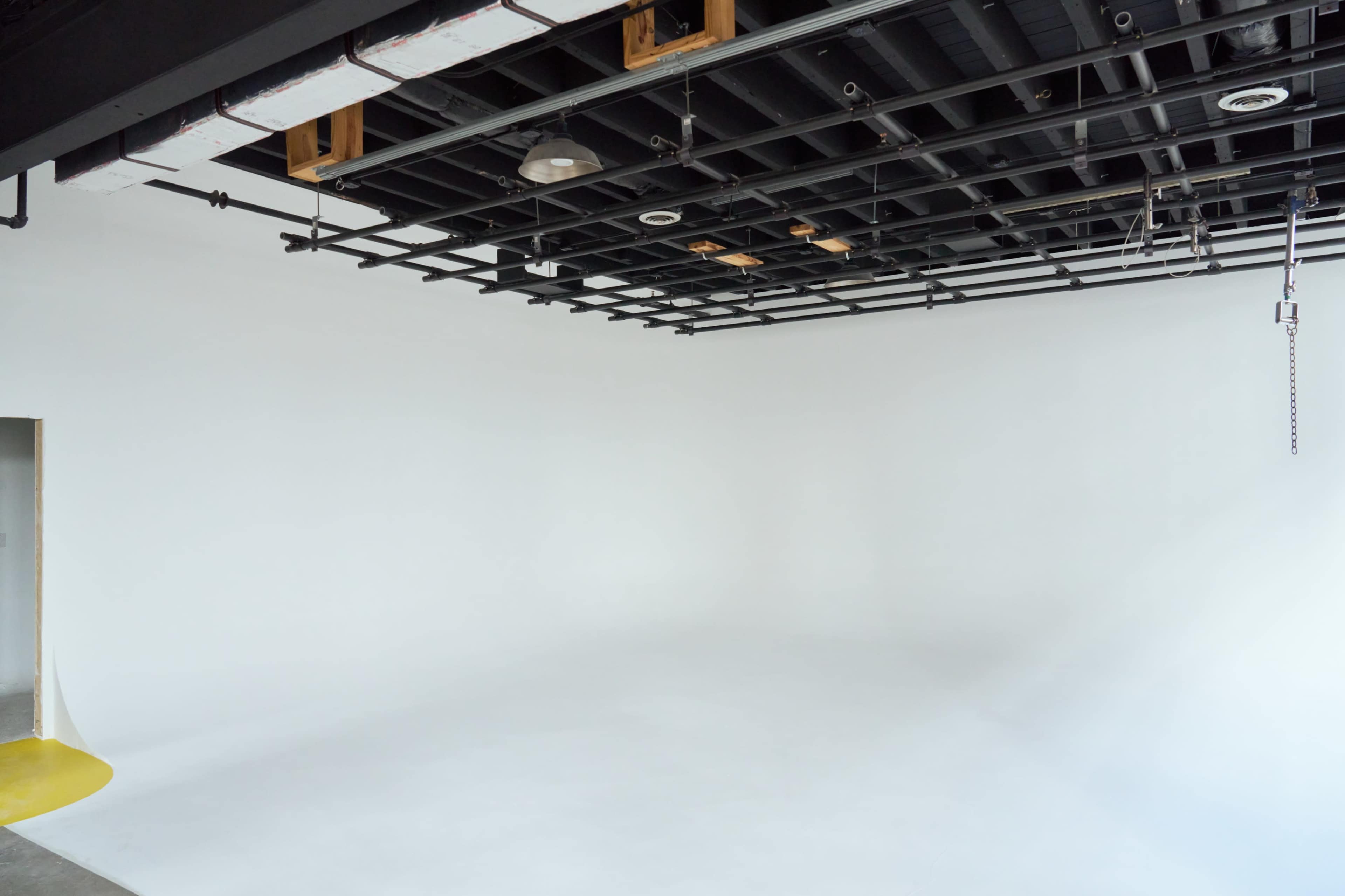 A spacious, empty studio with a white background and a black ceiling grid.