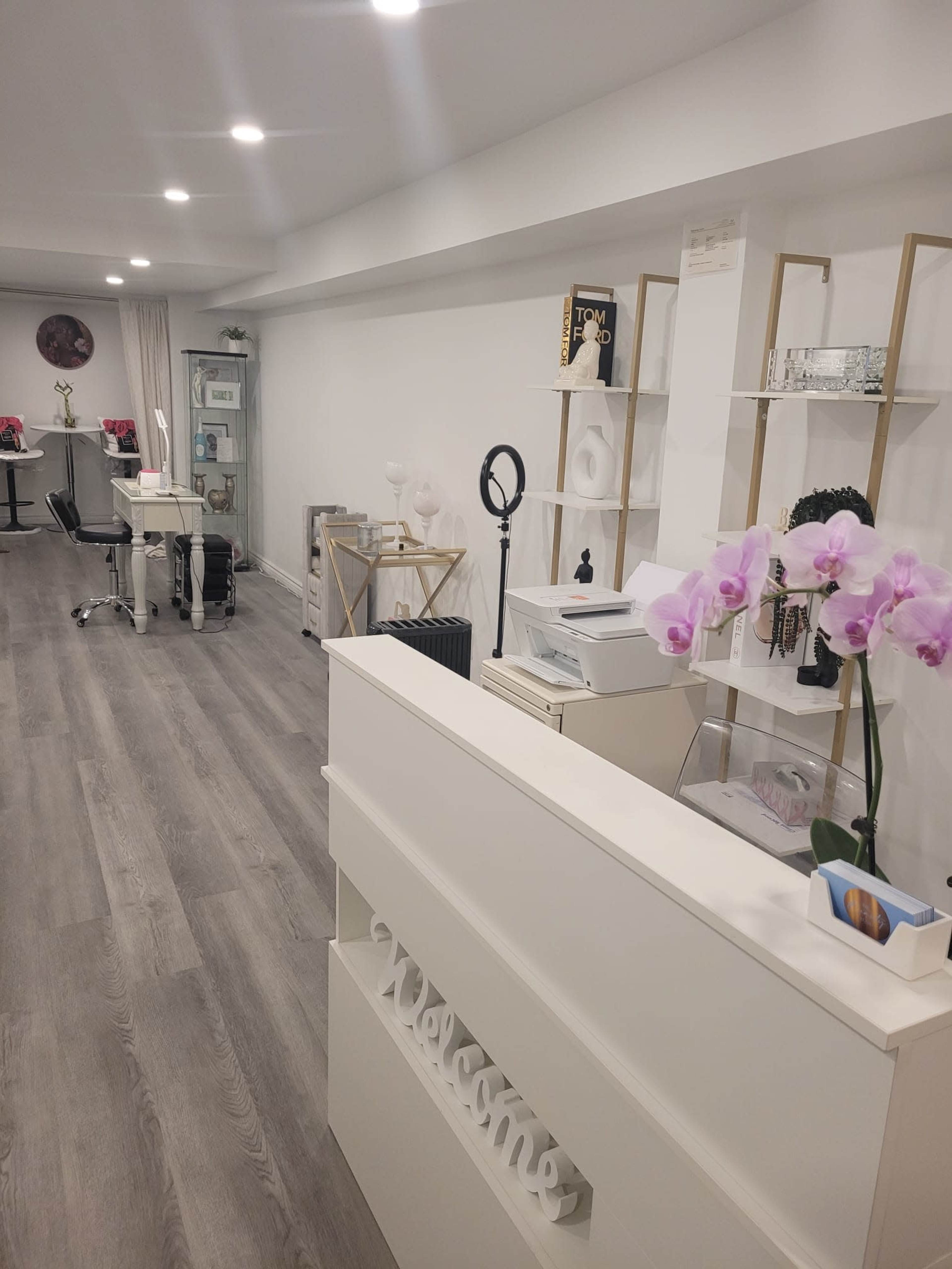 A modern reception area with a white desk, decorative shelves, and a setup for beauty services.