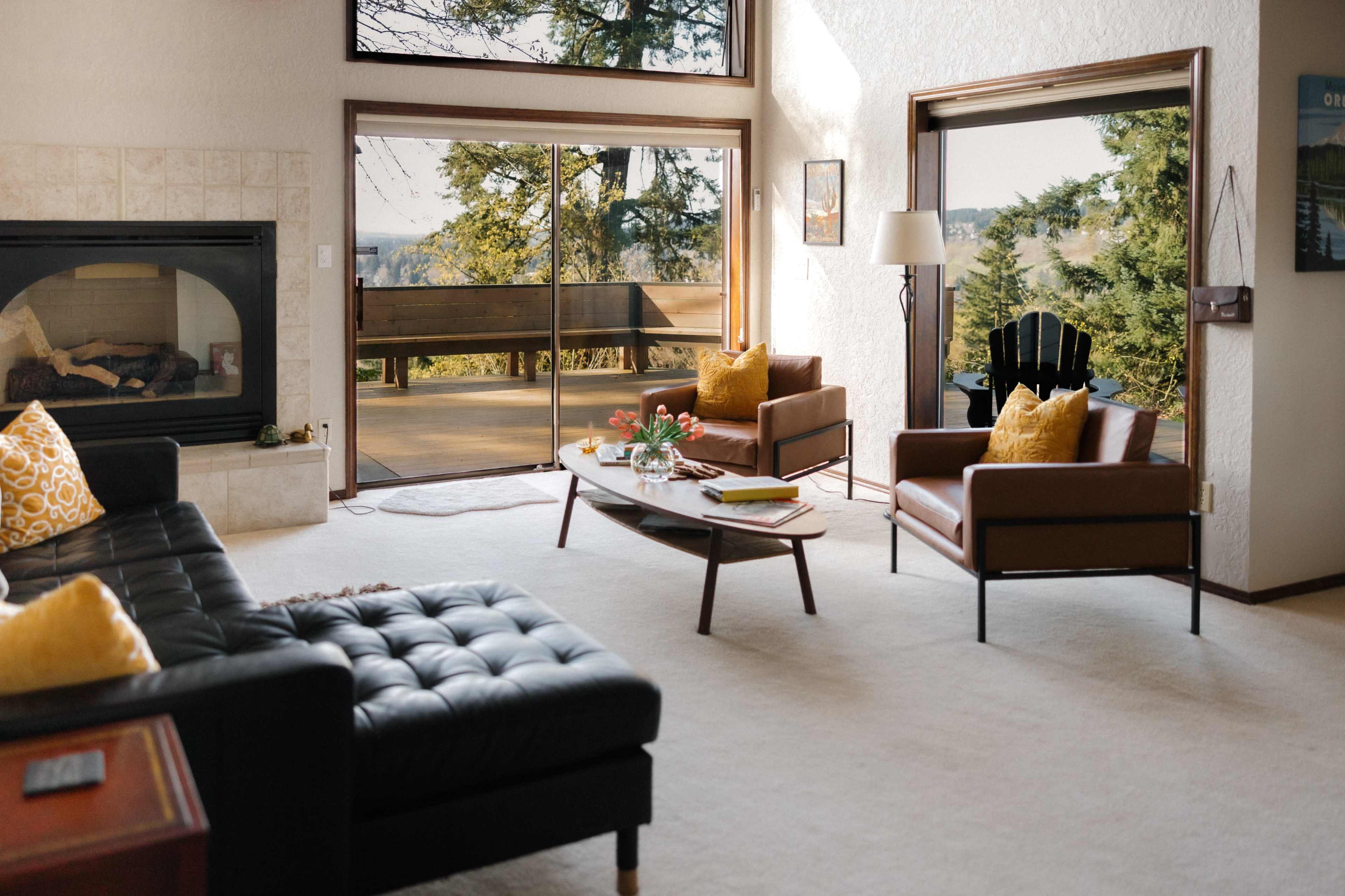 A modern living room features a fireplace, two leather armchairs, and large sliding doors that open to a scenic view.