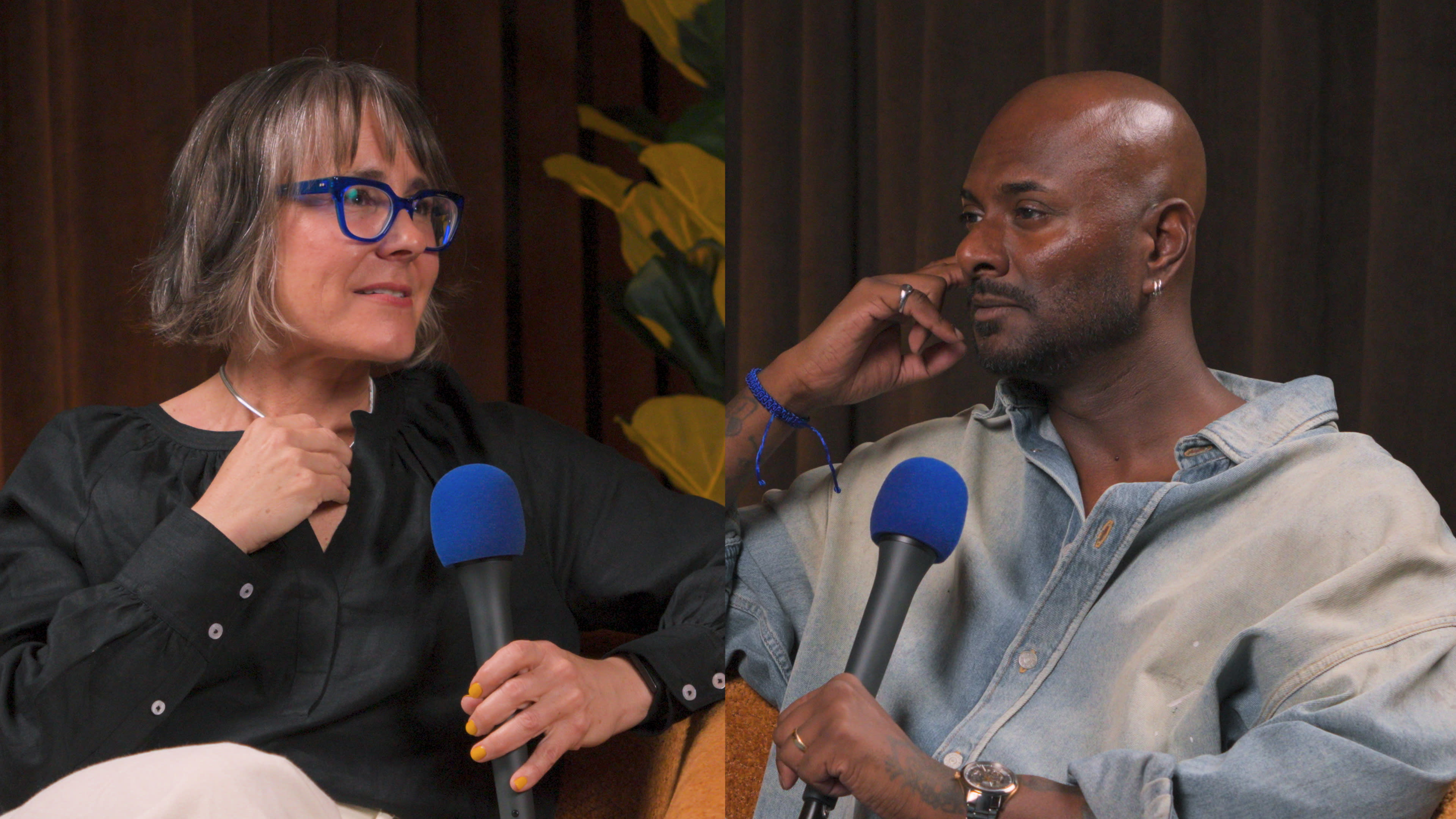 A woman and a man participate in a conversation, each holding a microphone, with a backdrop of yellow flowers.