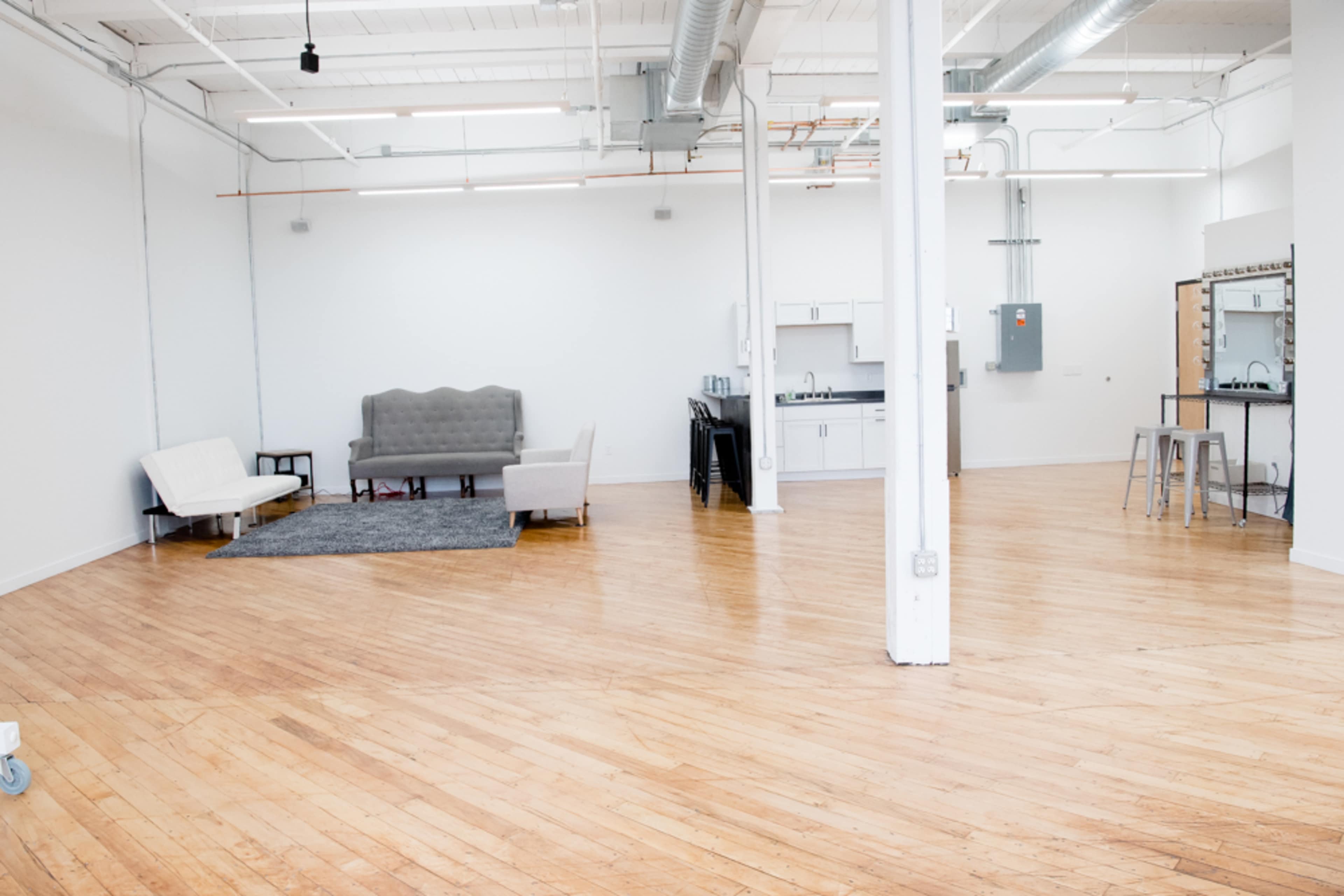 An empty commercial space featuring wooden flooring, a few seating areas, a kitchenette, and a mirror station.