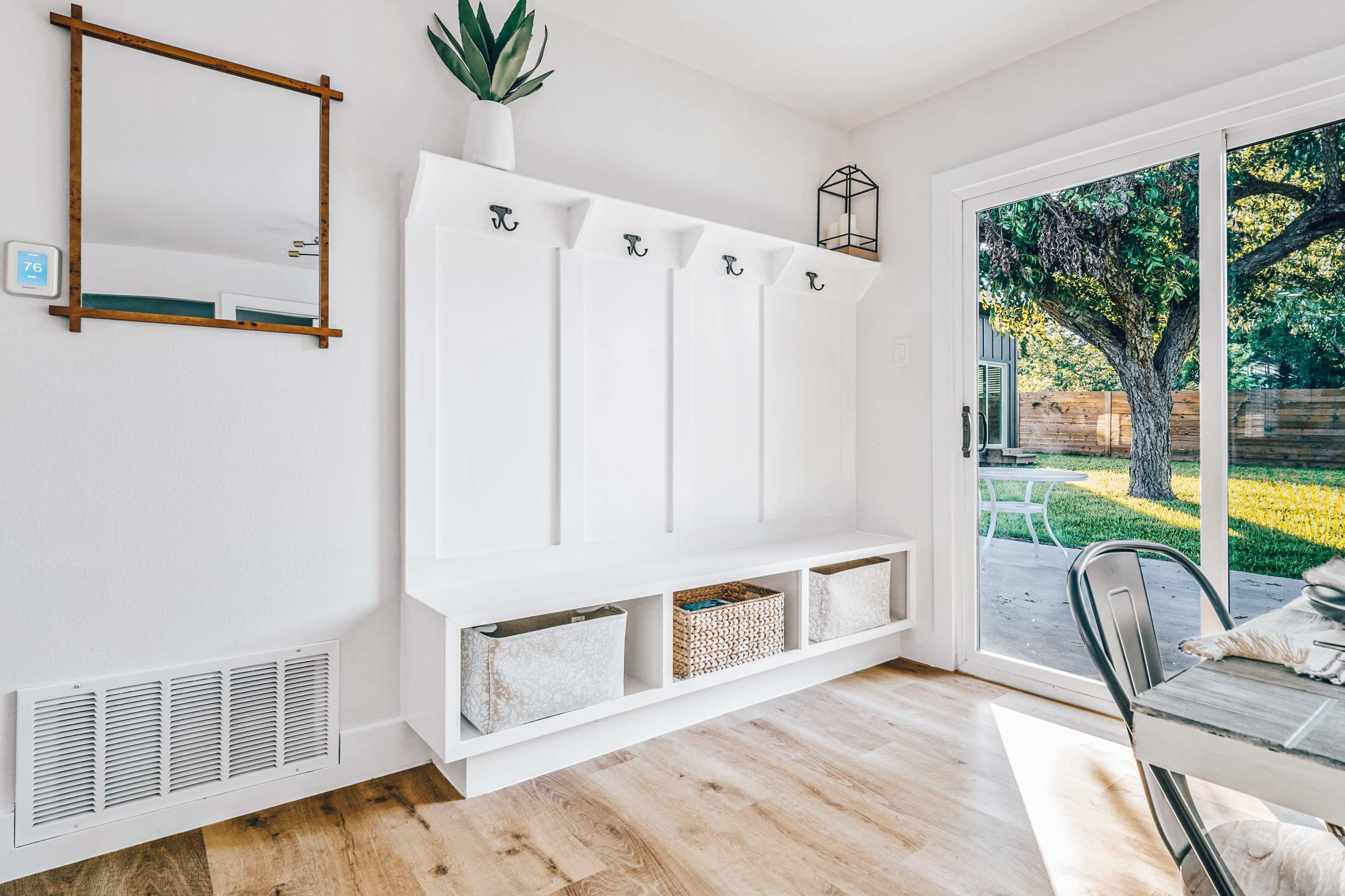 A modern entryway with a white wall-mounted coat rack, storage cubbies, and a view of a grassy backyard through sliding glass doors.