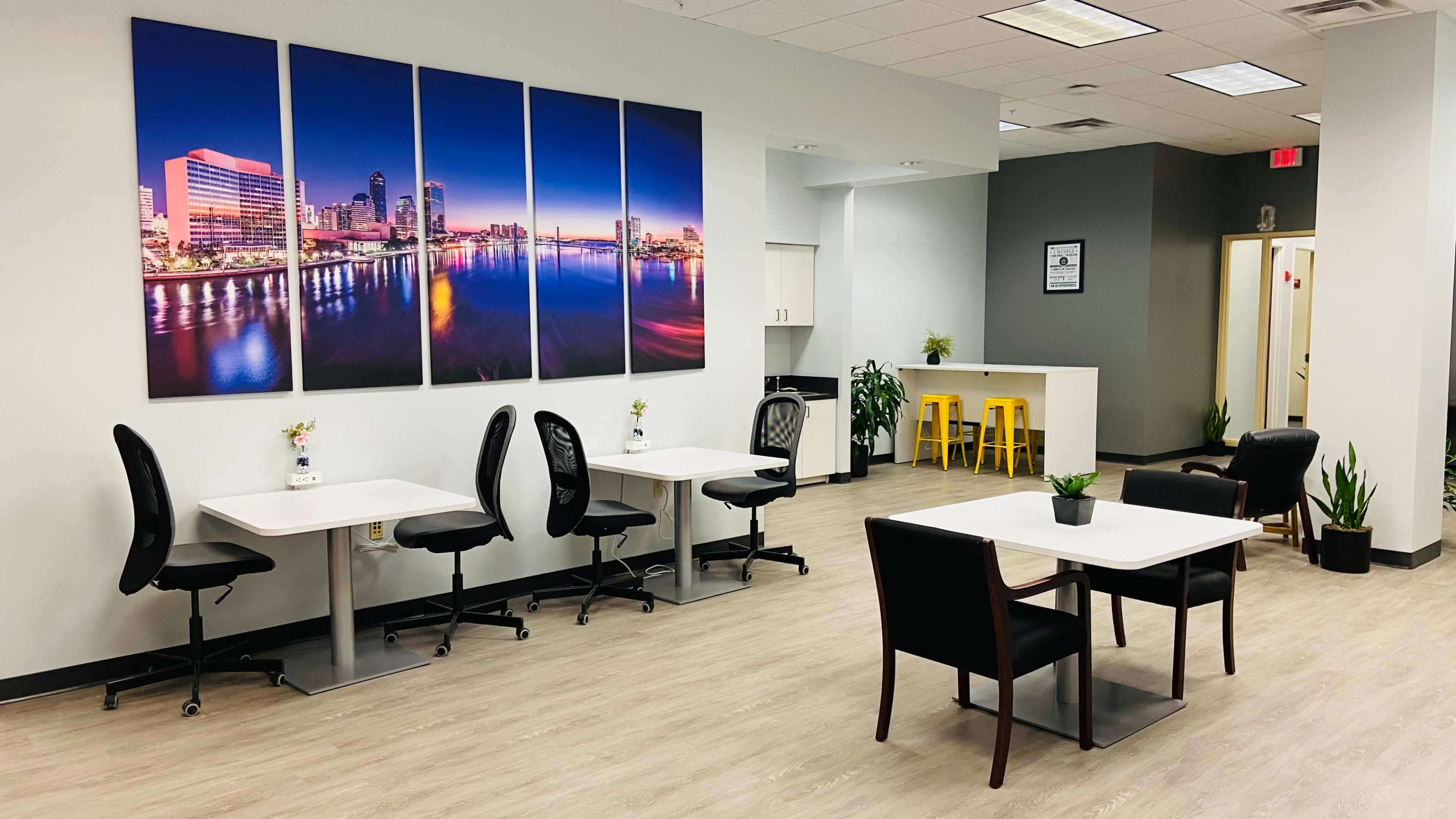 A modern office space with two tables and chairs, colorful artwork on the wall, and plants placed around the room.