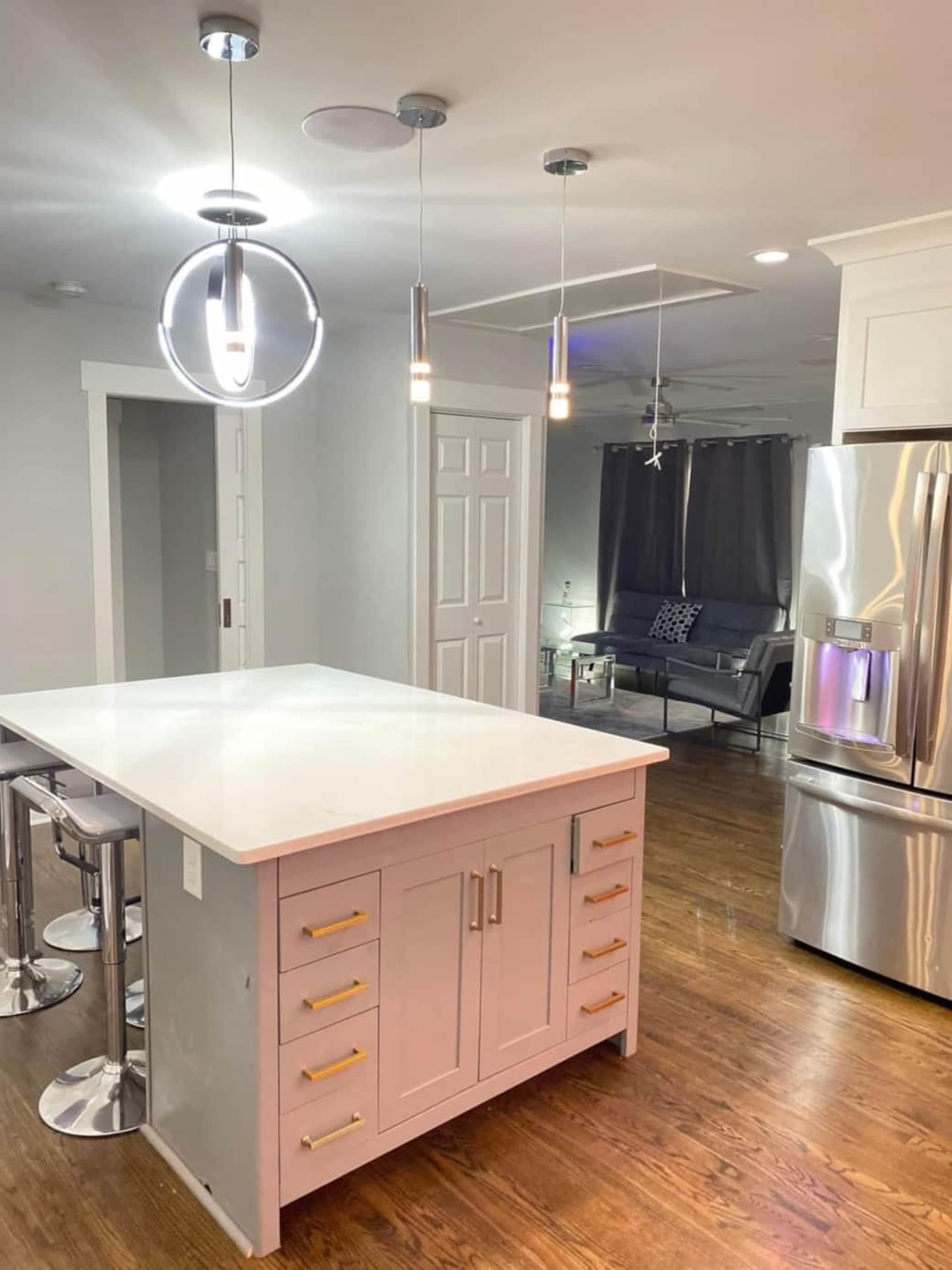 A modern kitchen features a central island with a white countertop, stainless steel appliances, and sleek pendant lighting.