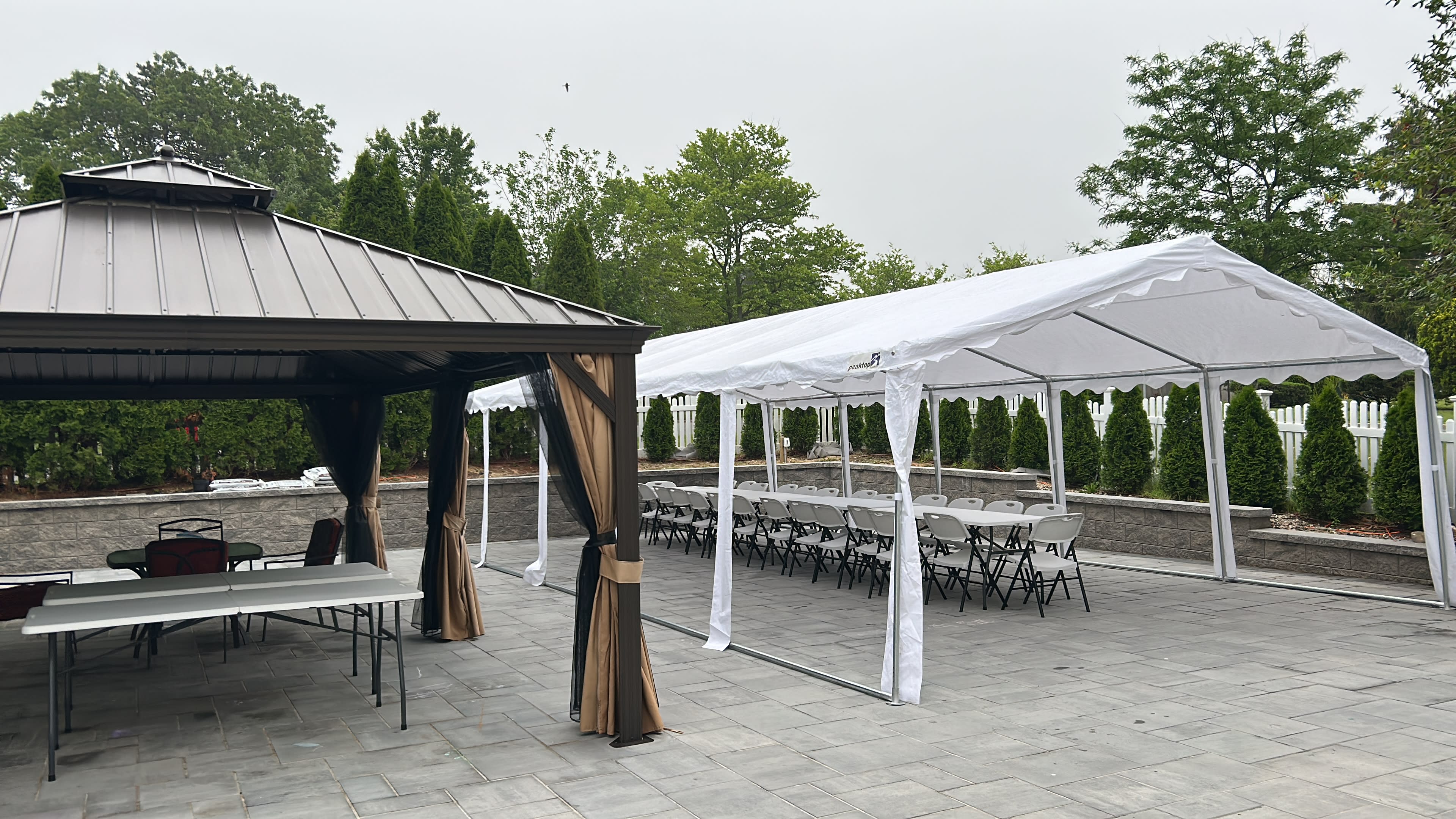 The image shows a patio area with a gazebo on the left and a white tent set up with rows of folding chairs on the right.