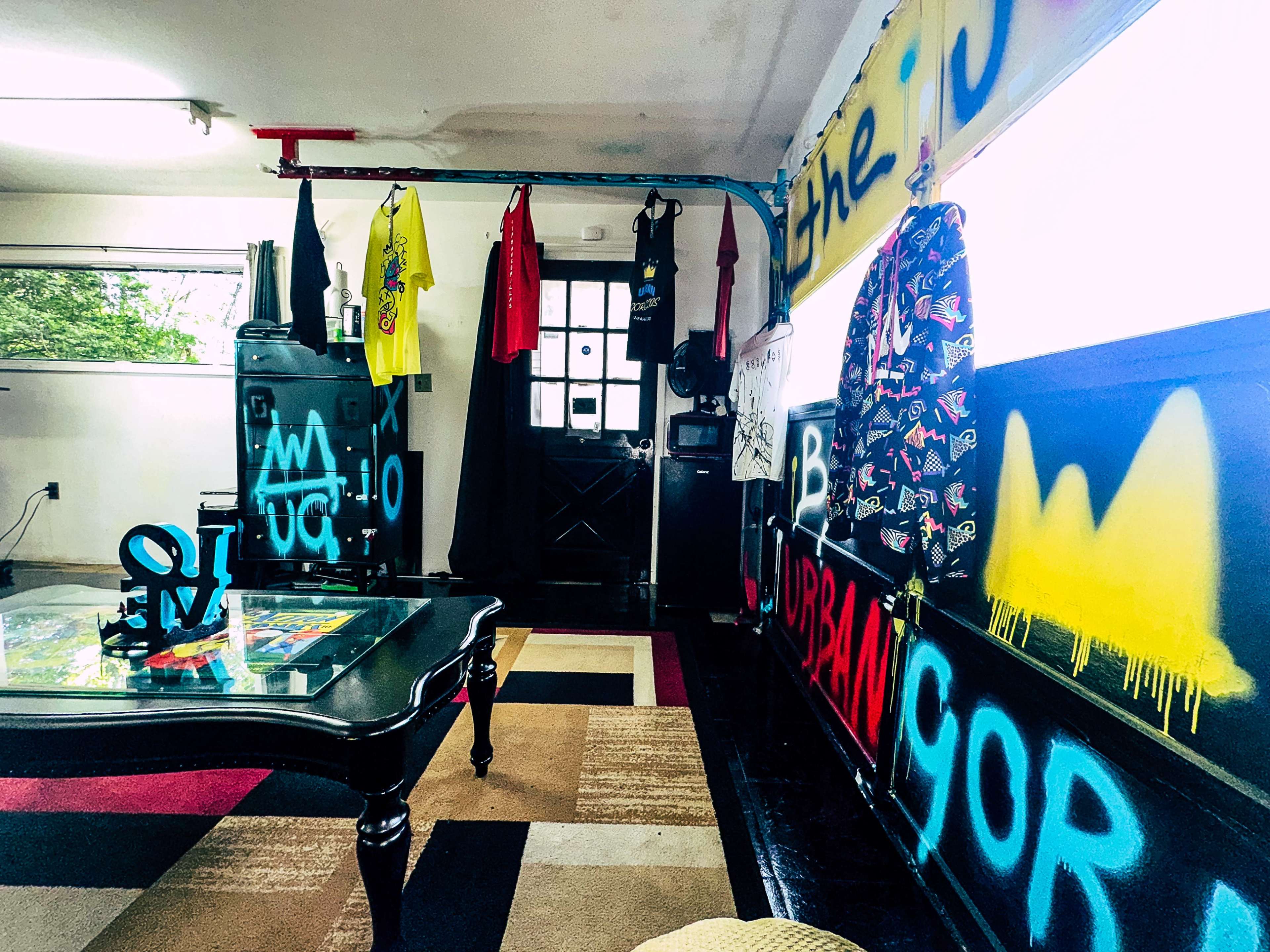 A room featuring colorful graffiti on the walls, various clothes hanging from a line, and a black coffee table in the center.