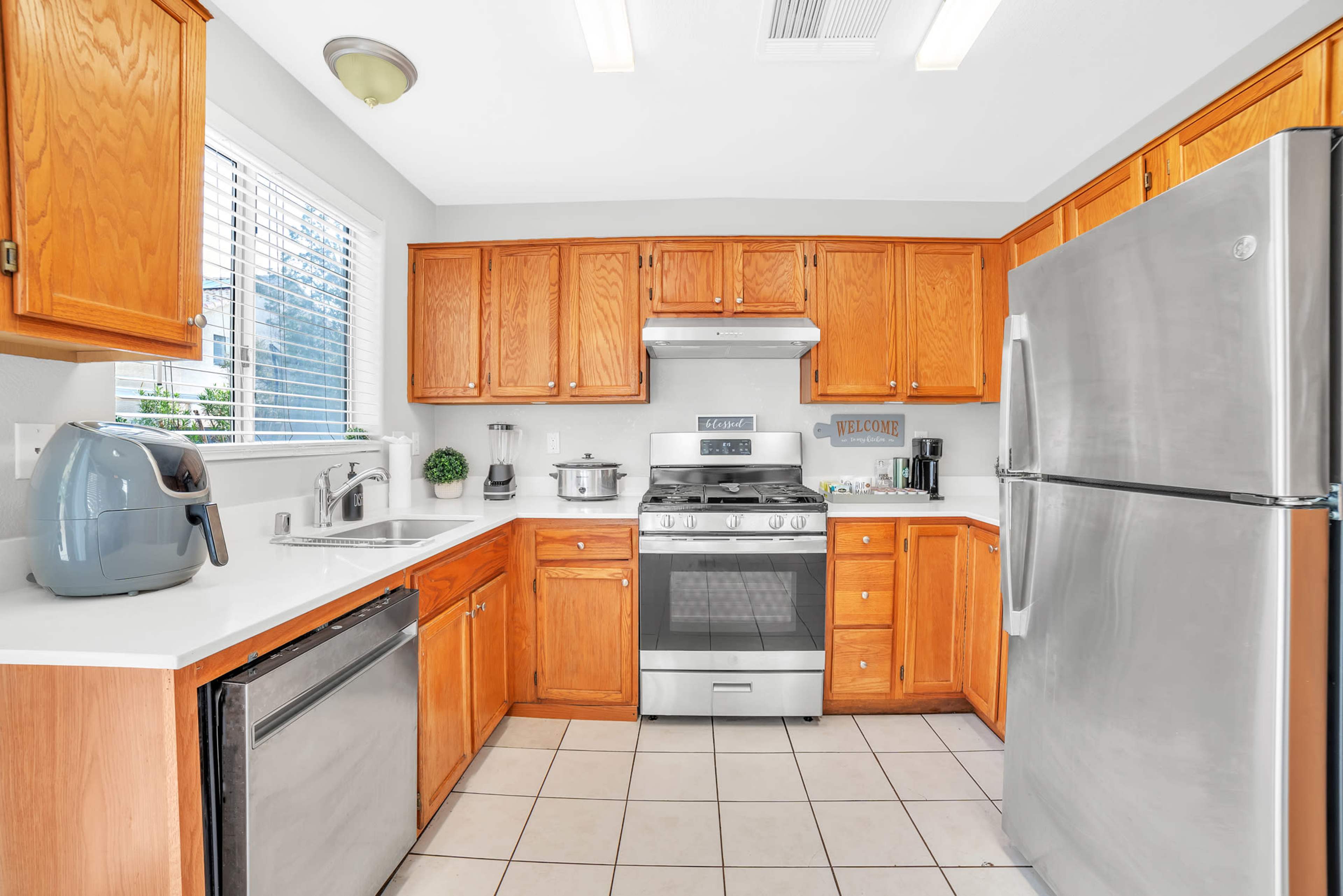 A kitchen with wooden cabinets, a stainless steel stove and refrigerator, and a tiled floor.