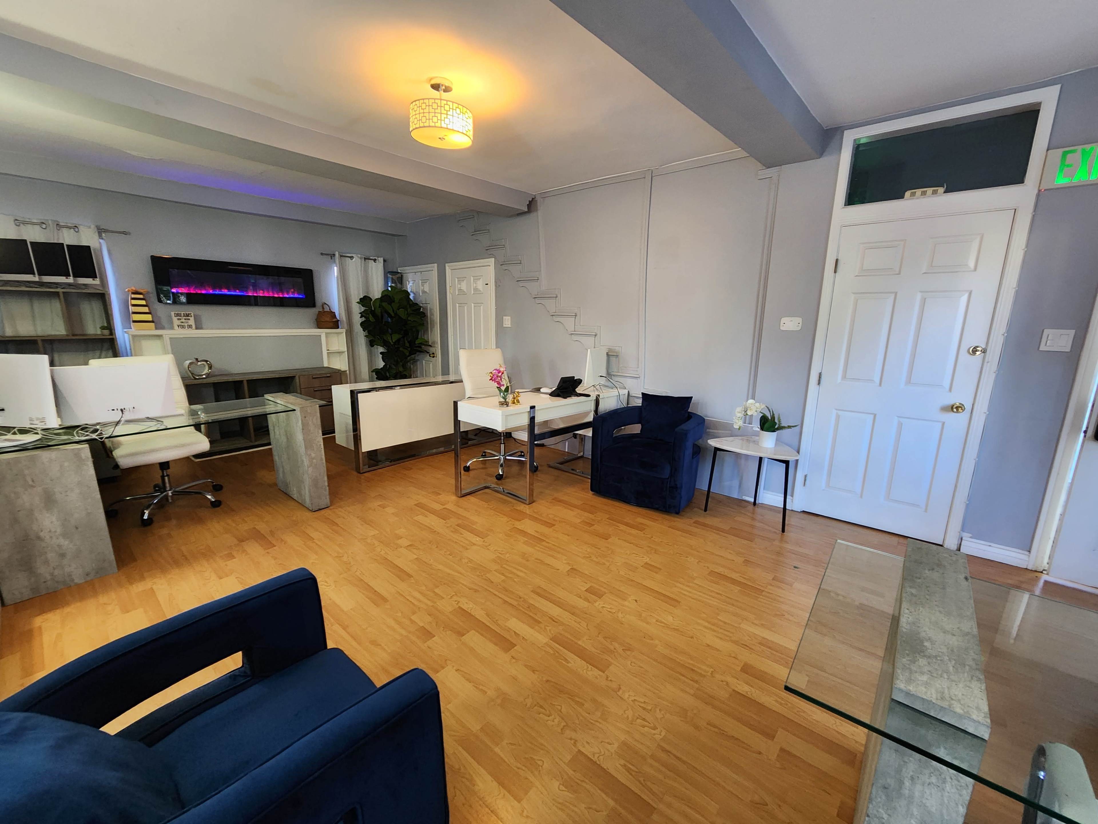 The image shows a modern office space with two desk areas, a seating arrangement, and a staircase in the background.