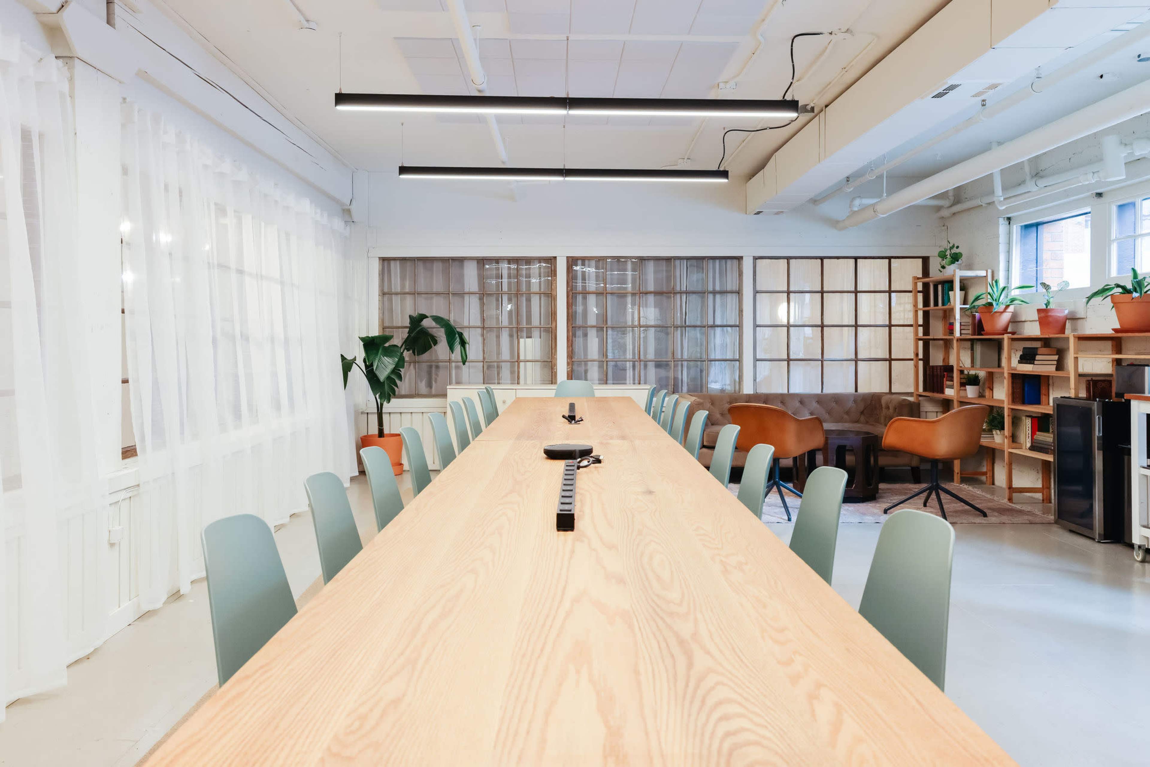 A long wooden table is set in a bright room with chairs, plants, and bookshelves in the background.