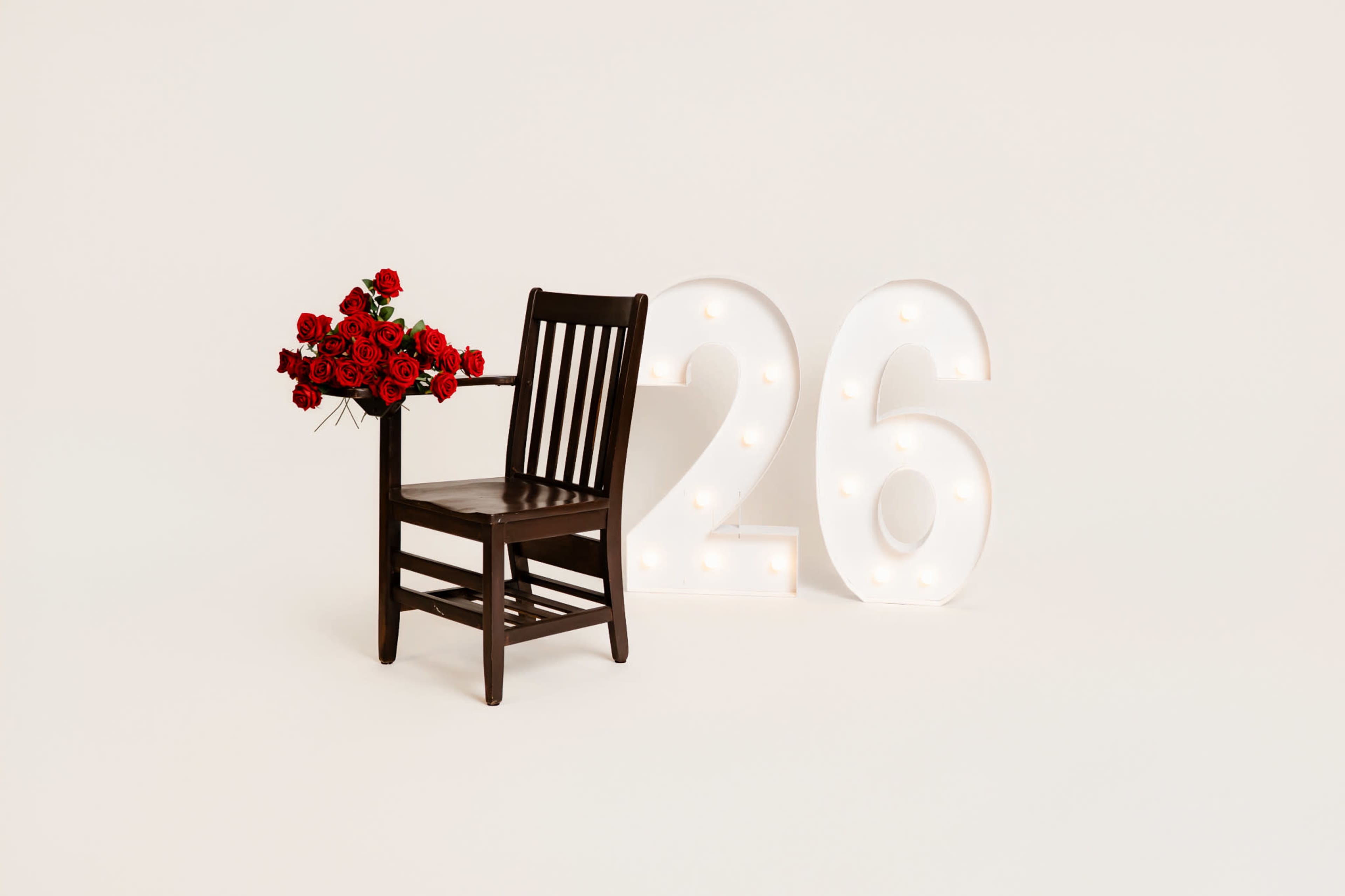 A wooden chair with a bouquet of red roses is placed next to large illuminated numbers reading "26."