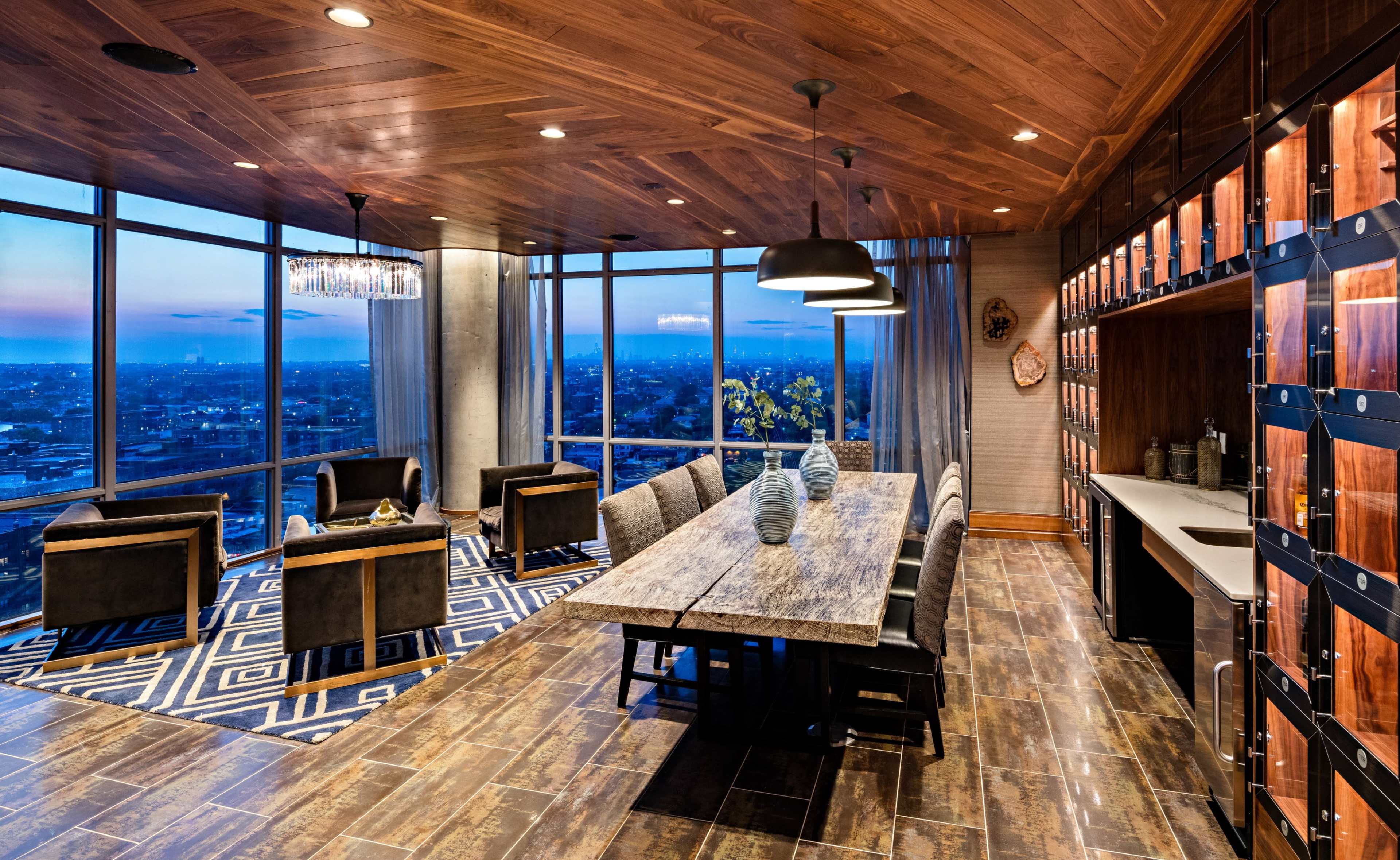 A modern conference room with a large wooden table, several black chairs, and floor-to-ceiling windows offering a view of the city at dusk.