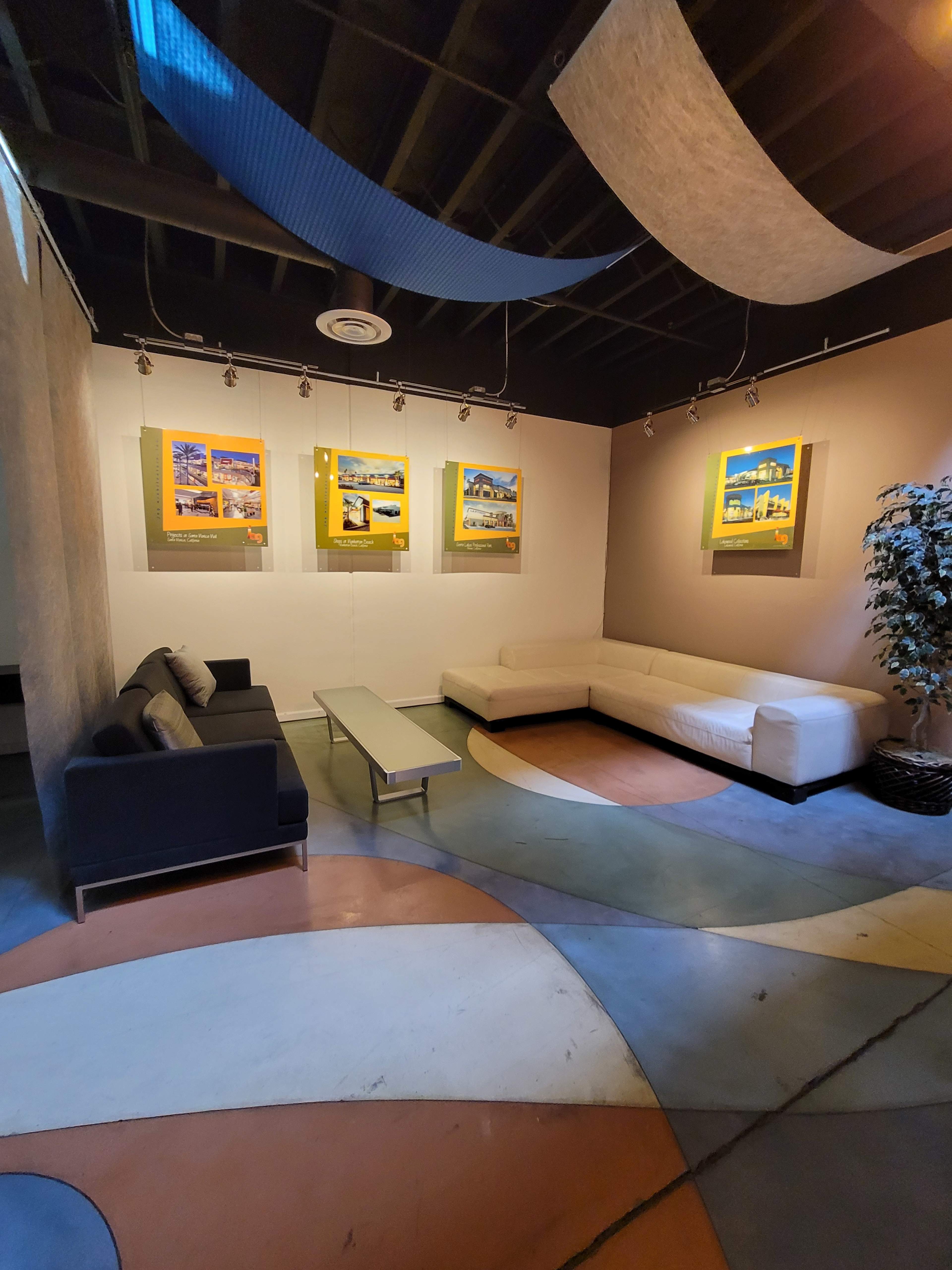 A modern lounge area with a black sofa, a white sectional couch, and colorful curved flooring, adorned with framed artwork on the walls.