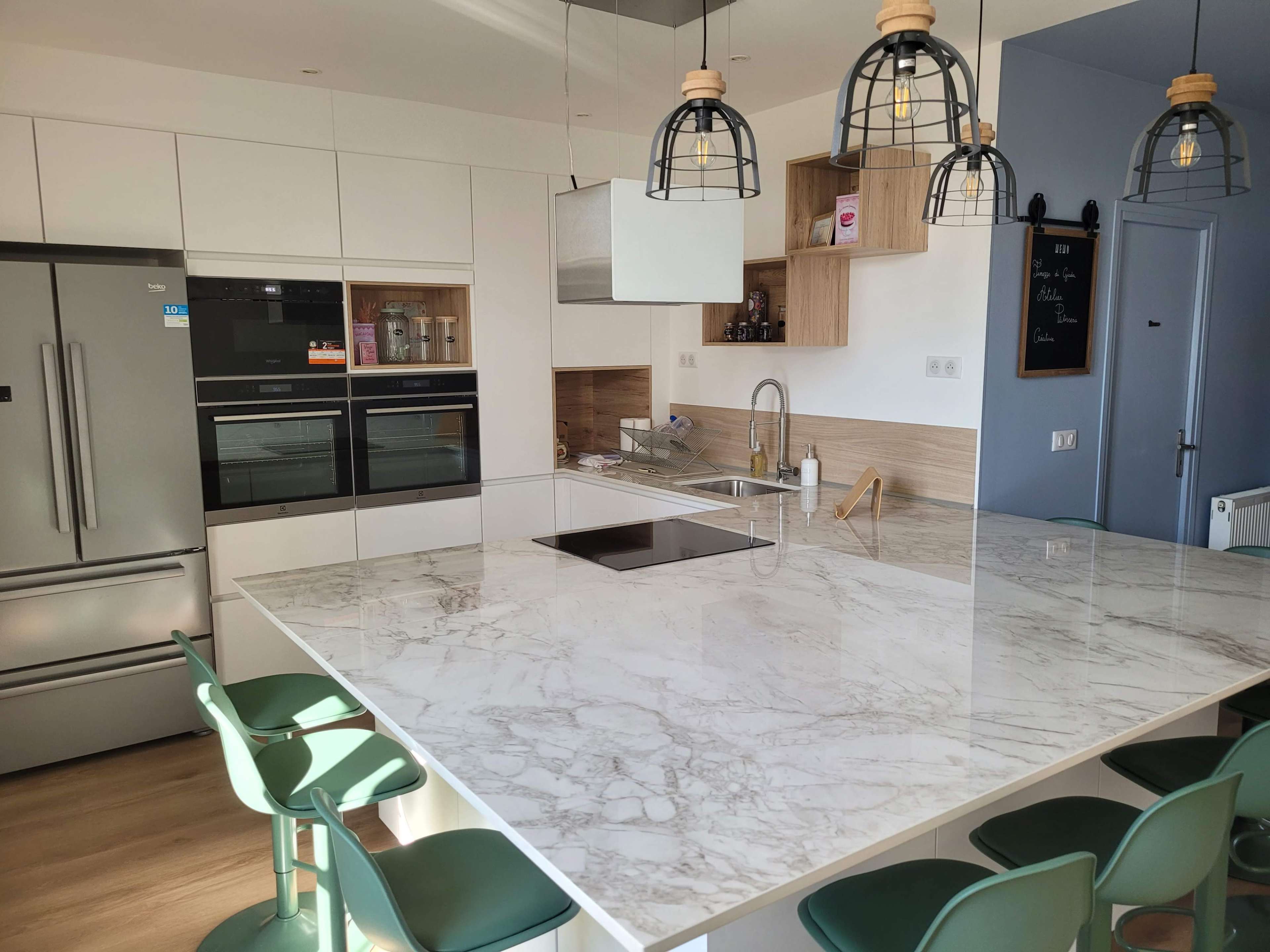 A modern kitchen with a marble countertop island, stainless steel appliances, and green bar stools.