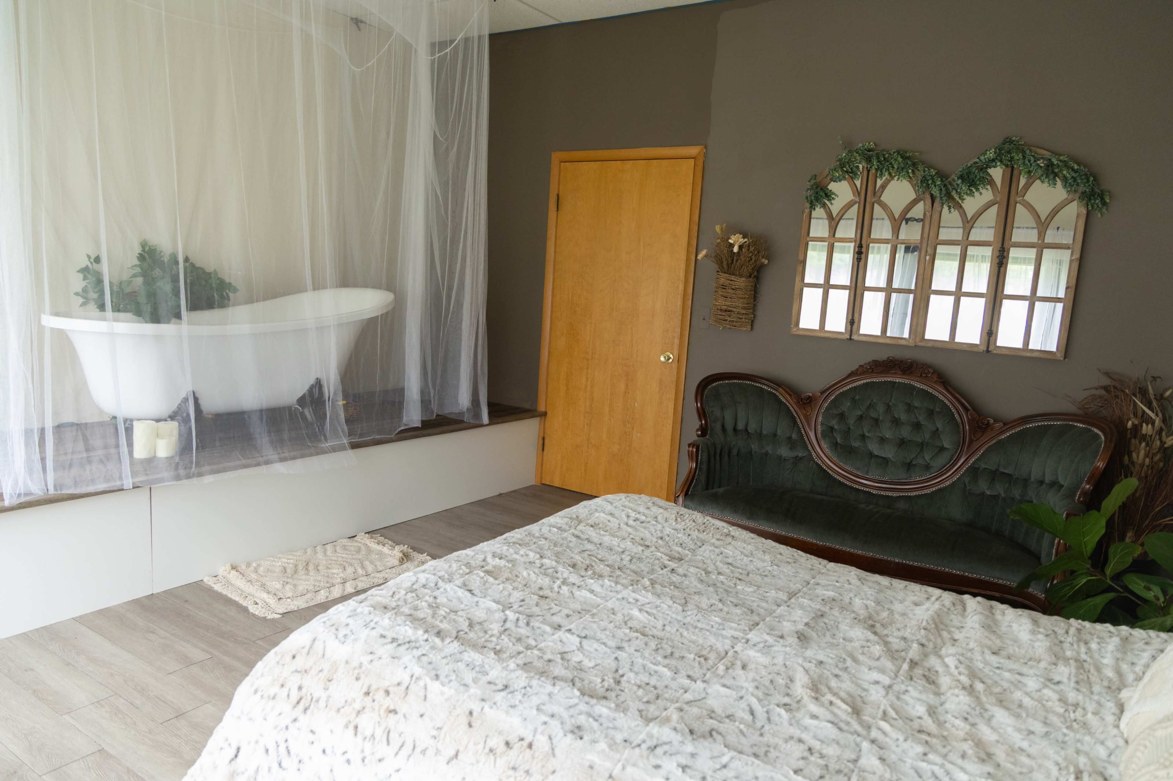 The image shows a cozy room featuring a vintage clawfoot bathtub on a raised platform, a plush green loveseat, and a textured rug on the floor.