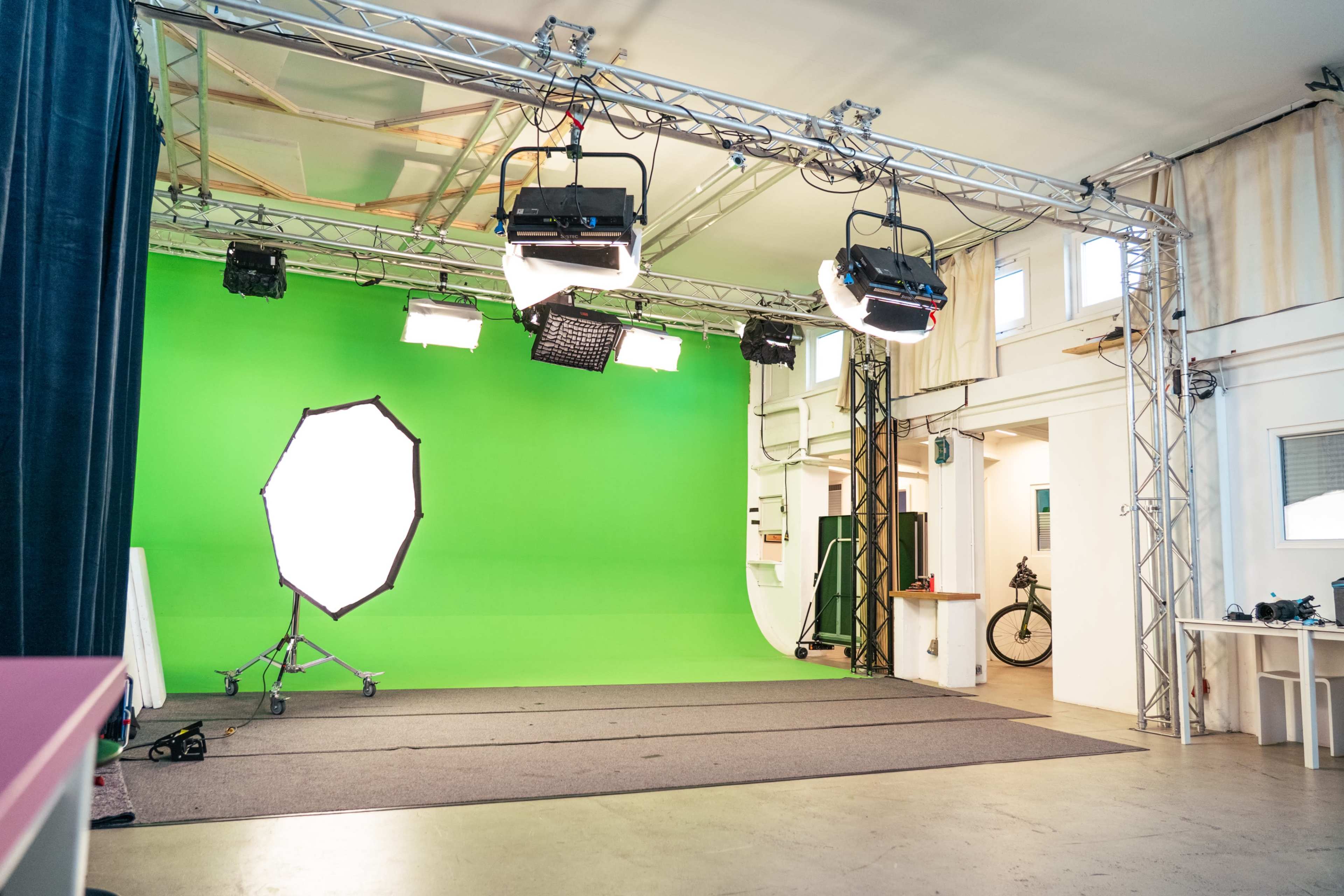 The image shows a photography studio equipped with a green screen backdrop and multiple lighting fixtures.