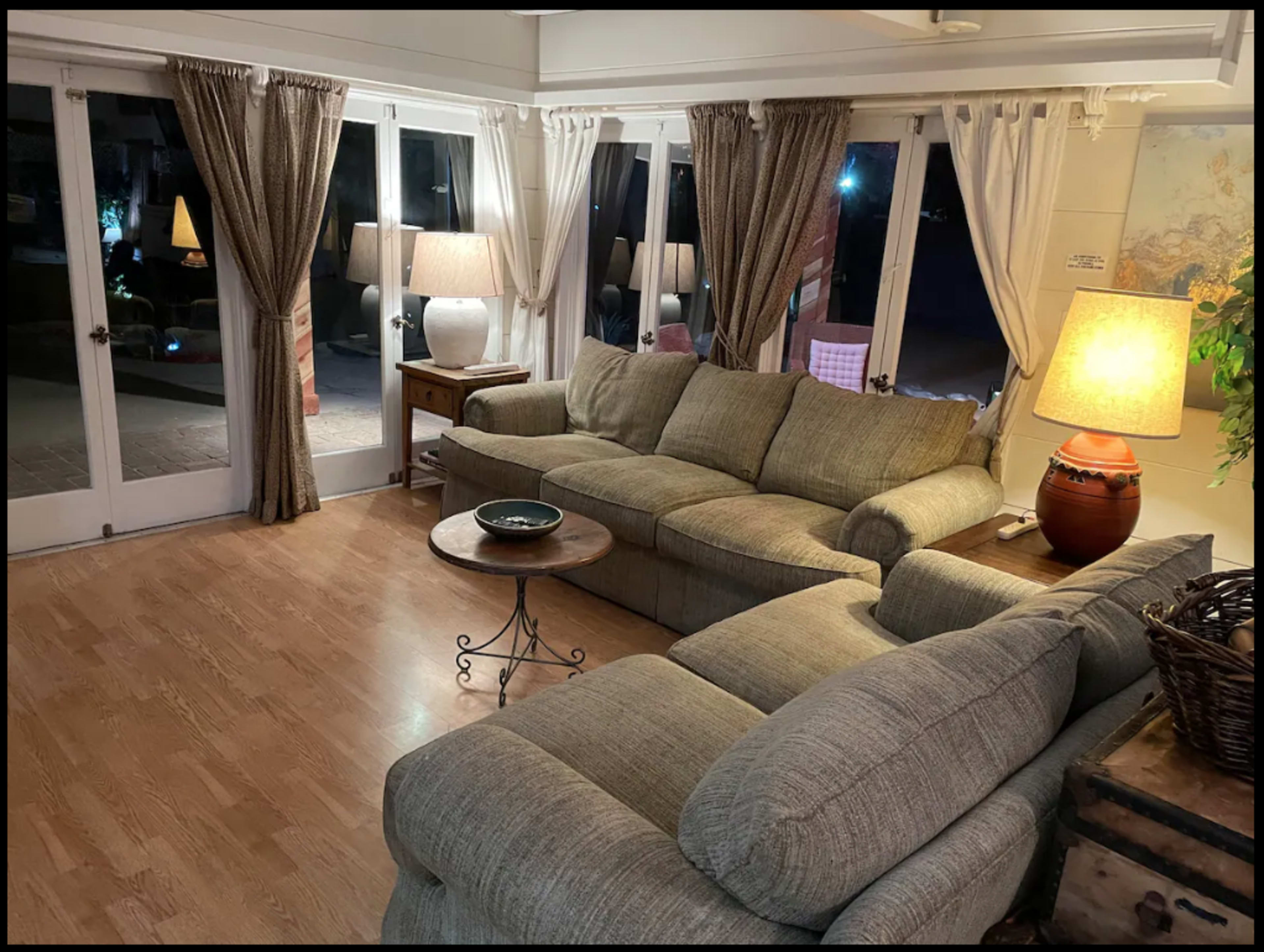 A living room with a sectional sofa, a round coffee table, and large windows covered with curtains.