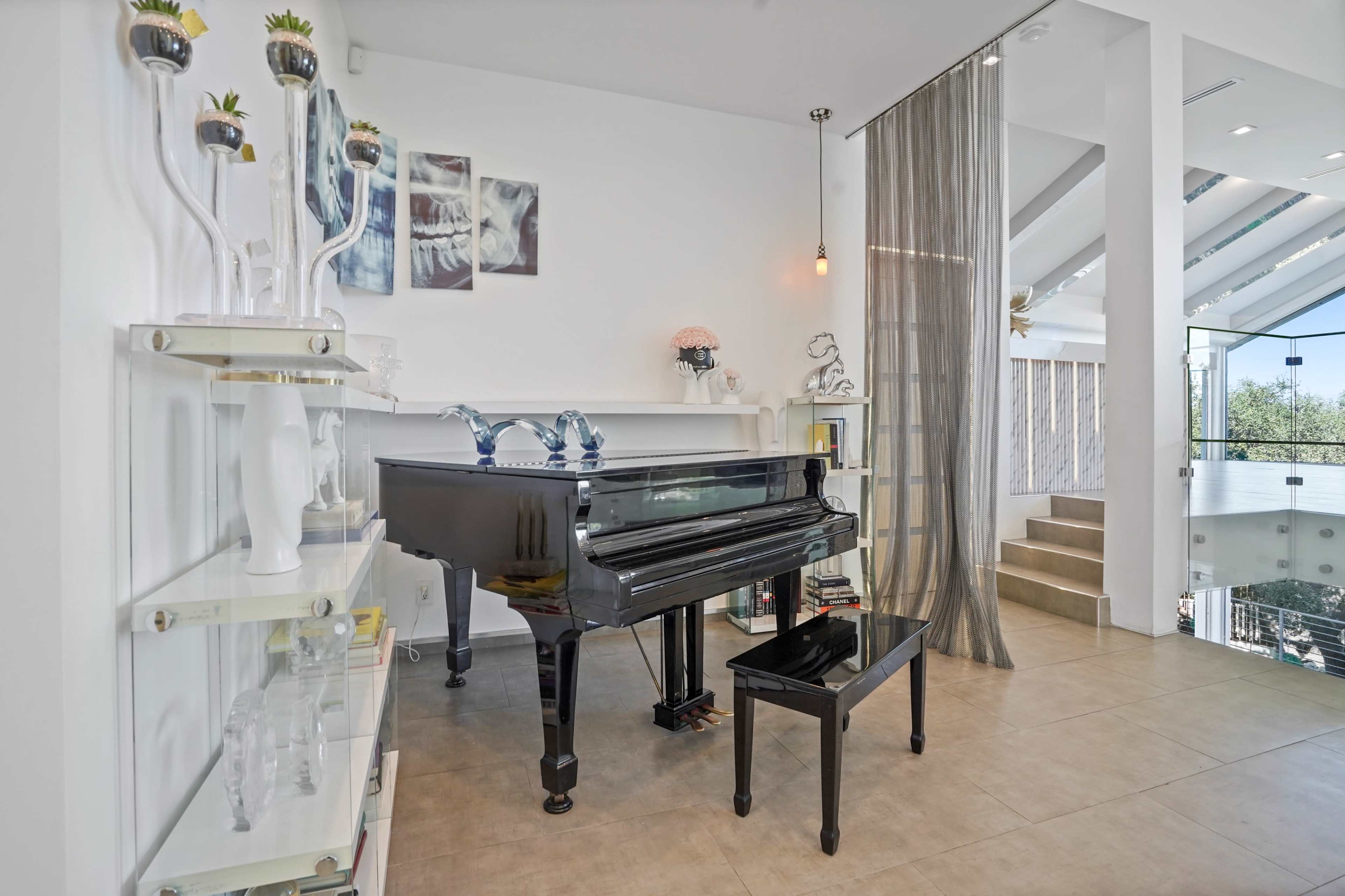 A black grand piano is positioned near a transparent curtain in a modern, well-lit room, with a staircase visible in the background.