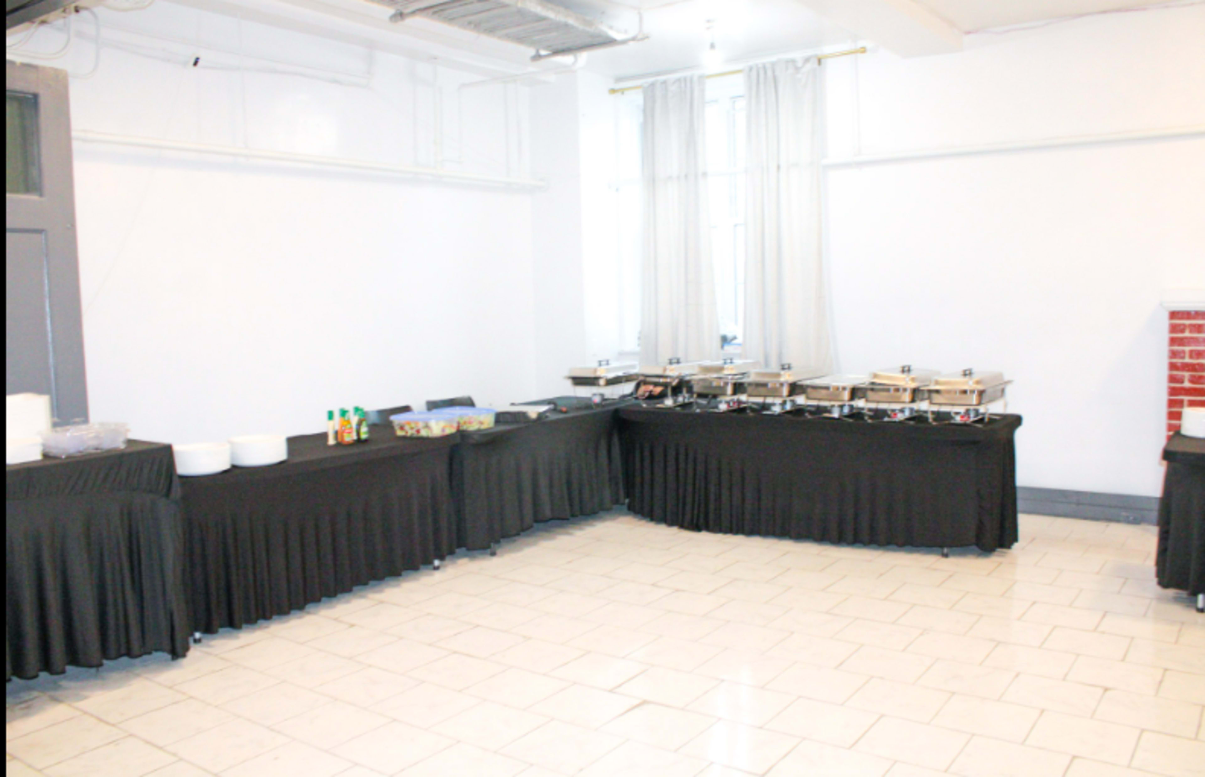 The image shows a spacious room with black tablecloths covering multiple tables set up for a buffet service, featuring serving trays and dishes.