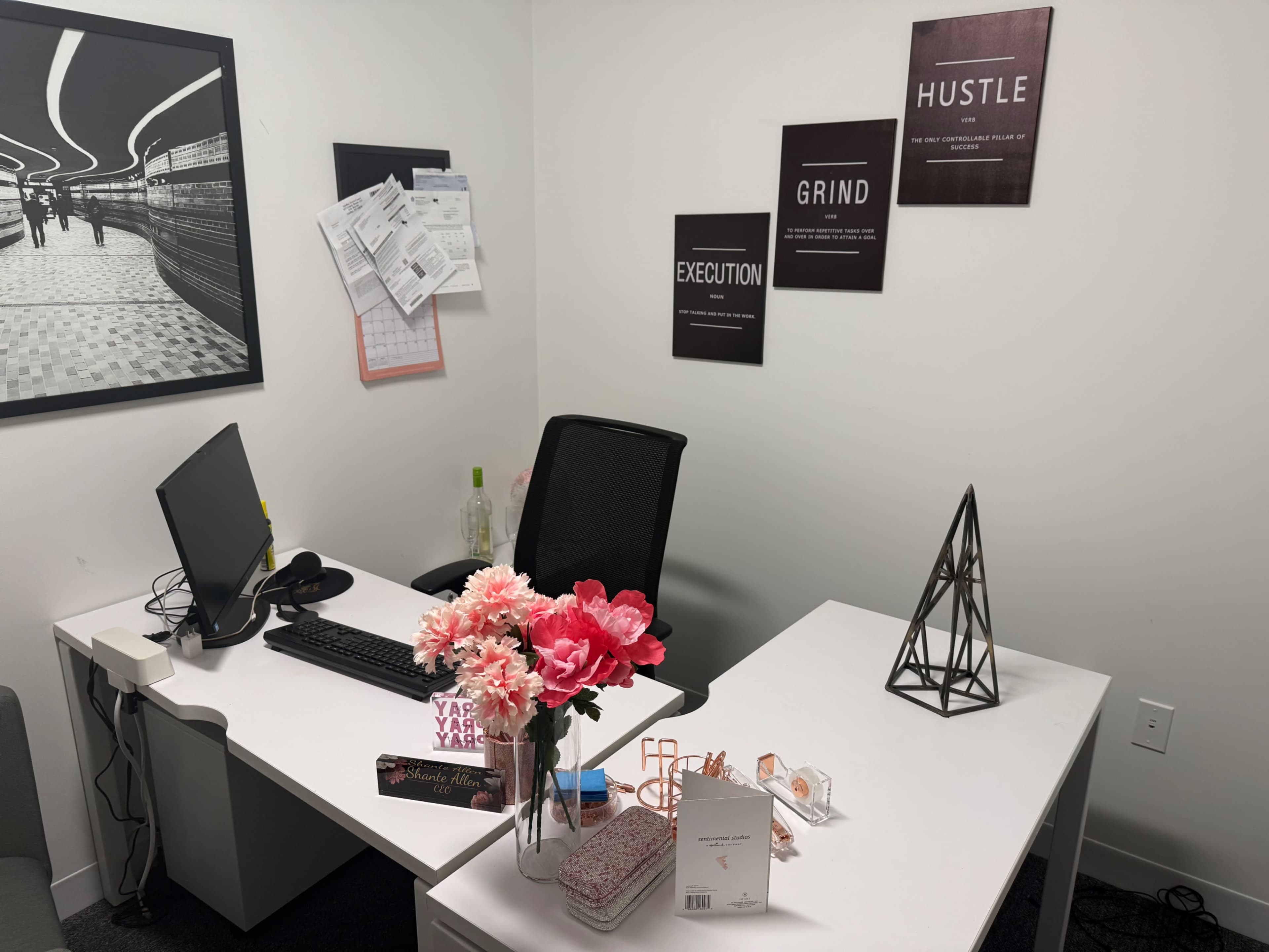 The image shows a modern office space featuring a desk with a computer, decorative flowers, a geometric sculpture, and motivational wall art.