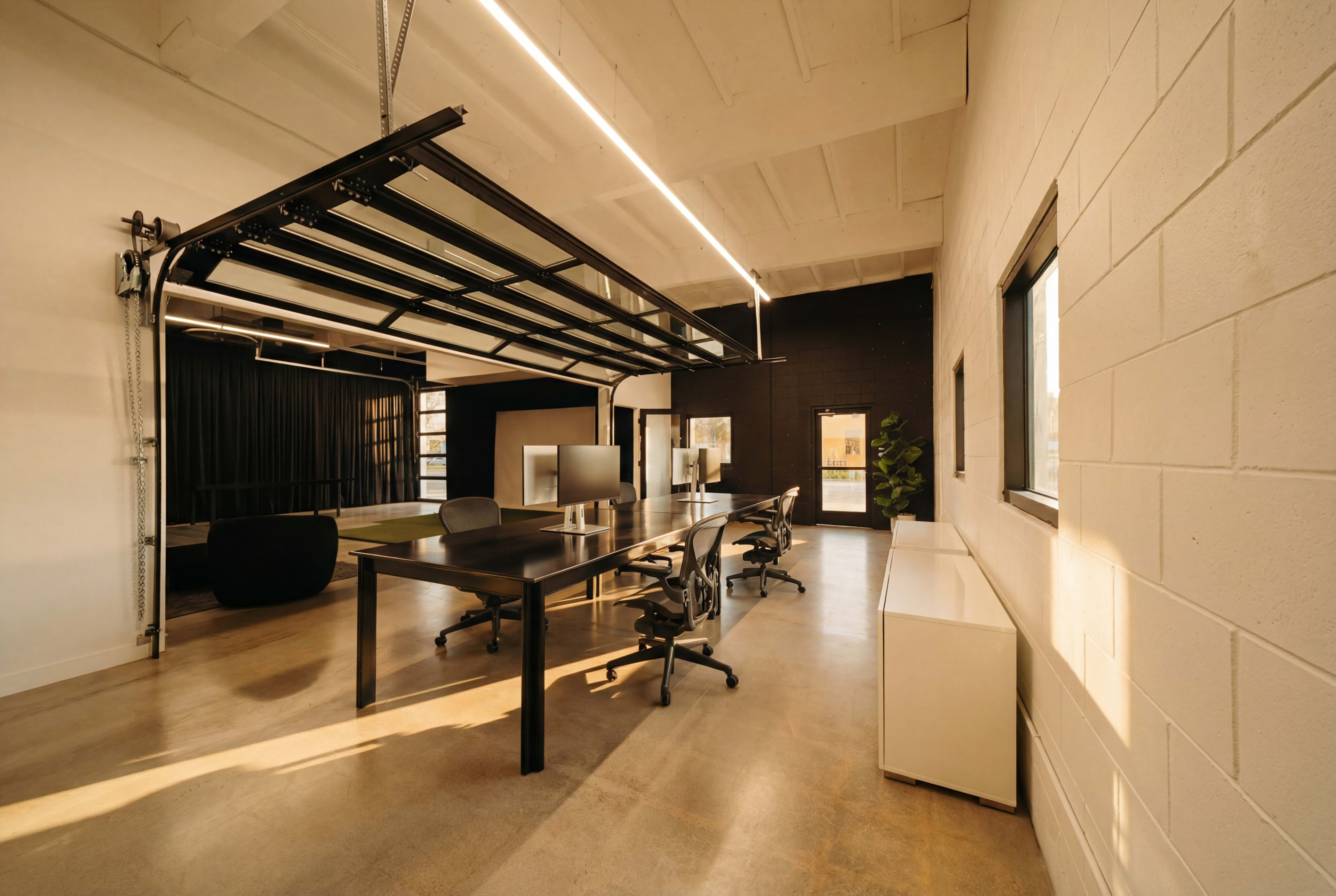 A modern office space features a large table with chairs, a glass wall, and minimalist decor.