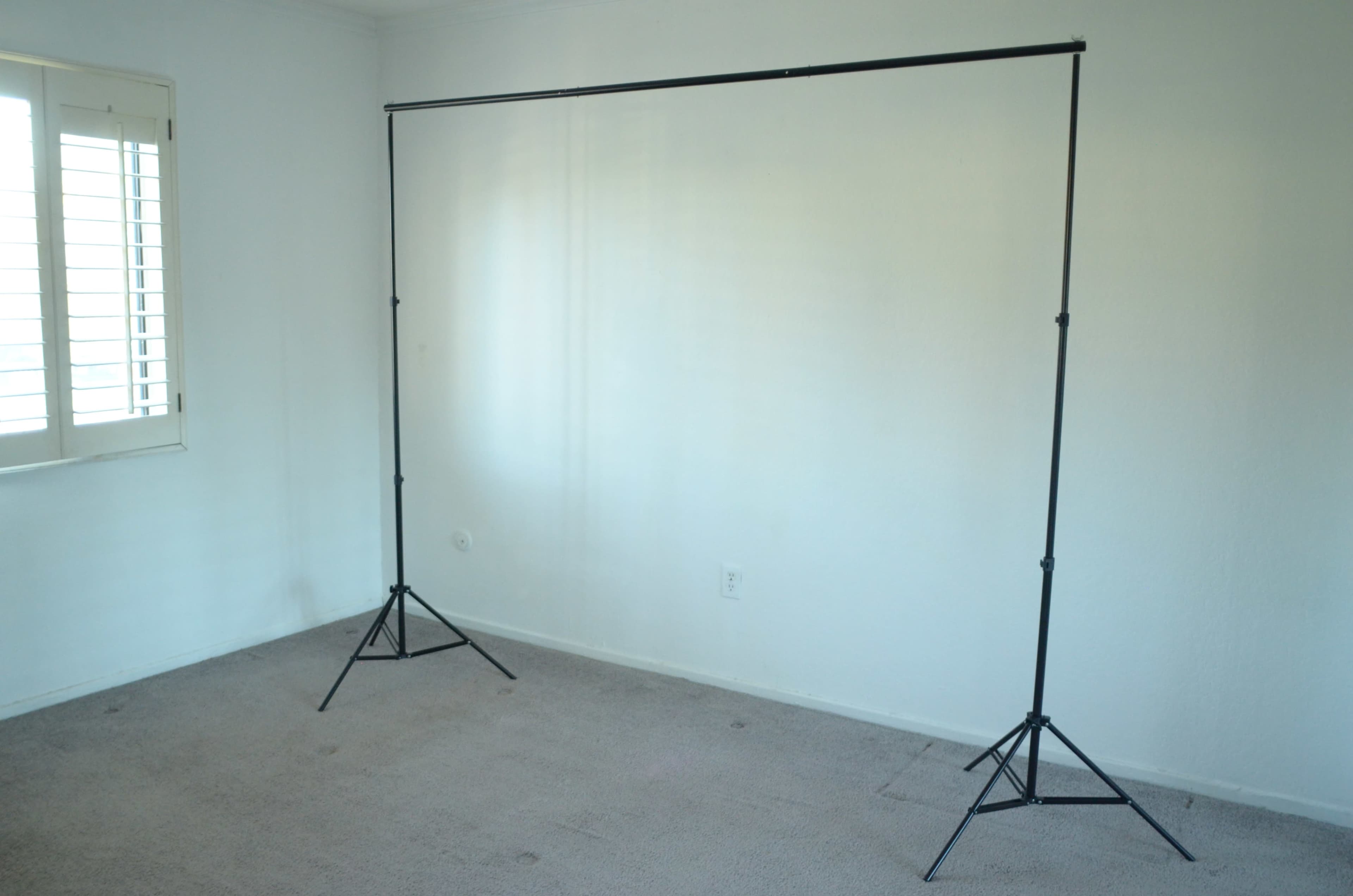 An empty room with beige carpet and a black backdrop stand set up in the center.