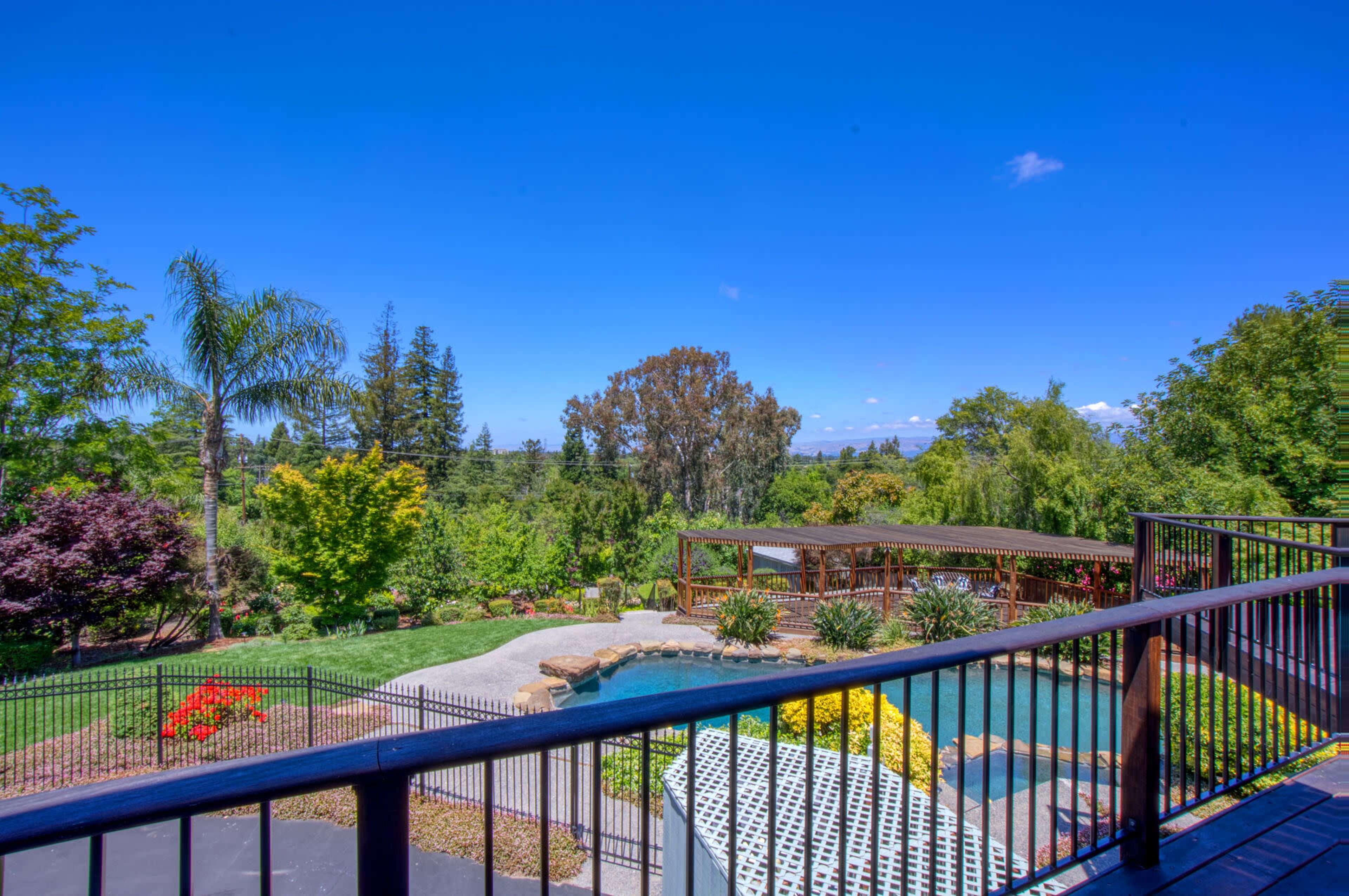 A backyard with a swimming pool, landscaped gardens, and trees under a clear blue sky.