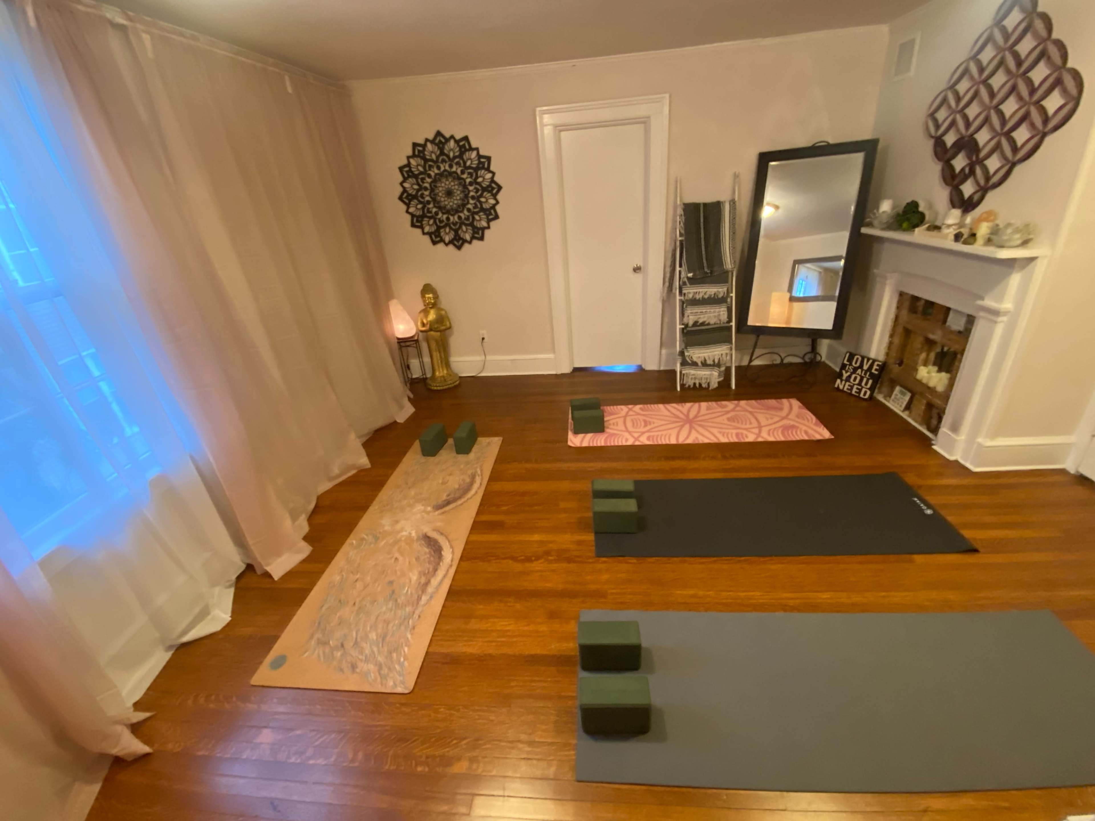 The image shows a yoga studio with several yoga mats arranged on the floor, blocks positioned beside them, and a serene decor featuring a large wall mirror and decorative elements.