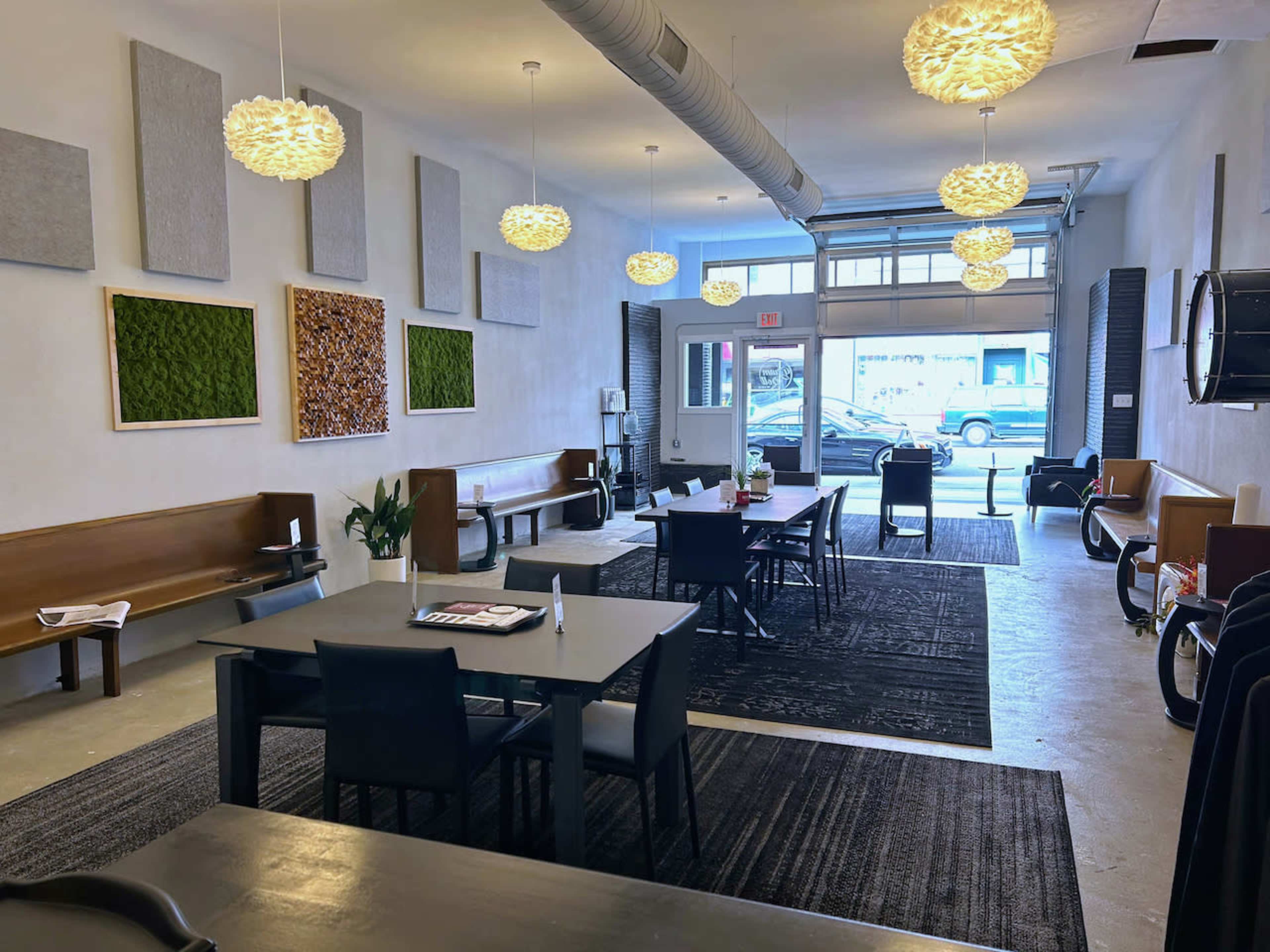 A modern indoor space with multiple dining tables, pendant lighting, and decorative wall elements made of moss and textured materials.