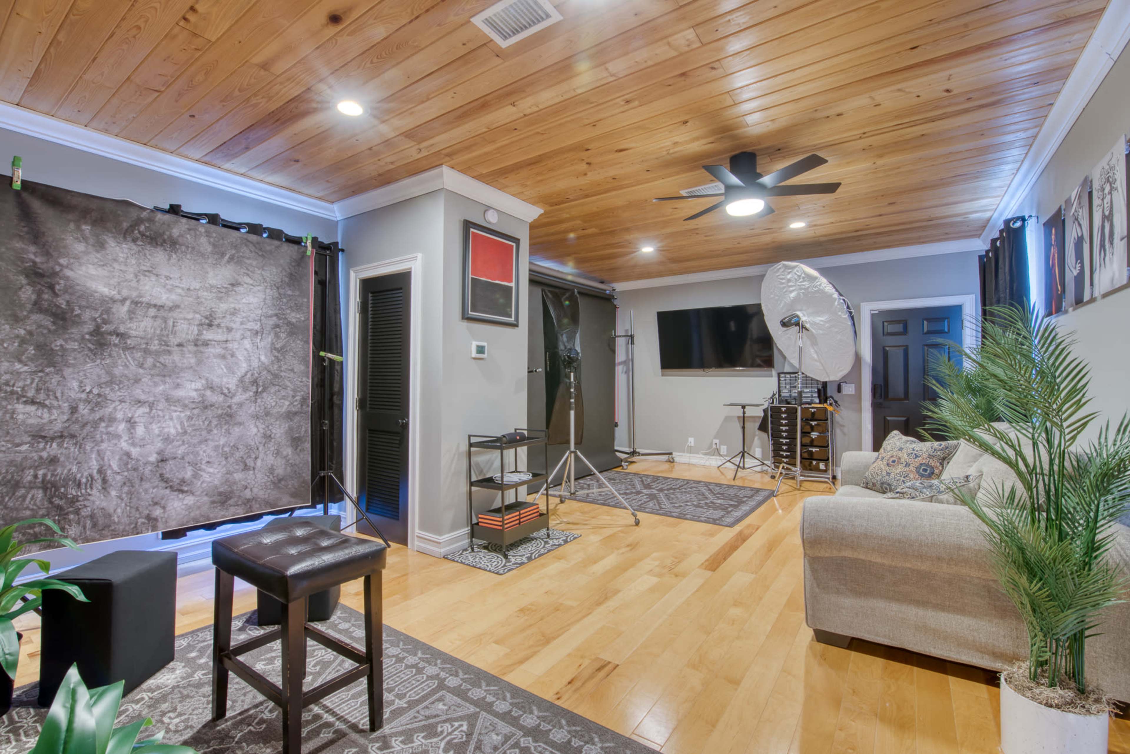 A well-lit photography studio featuring a sofa, backdrop stands, and studio equipment arranged on polished wooden flooring.