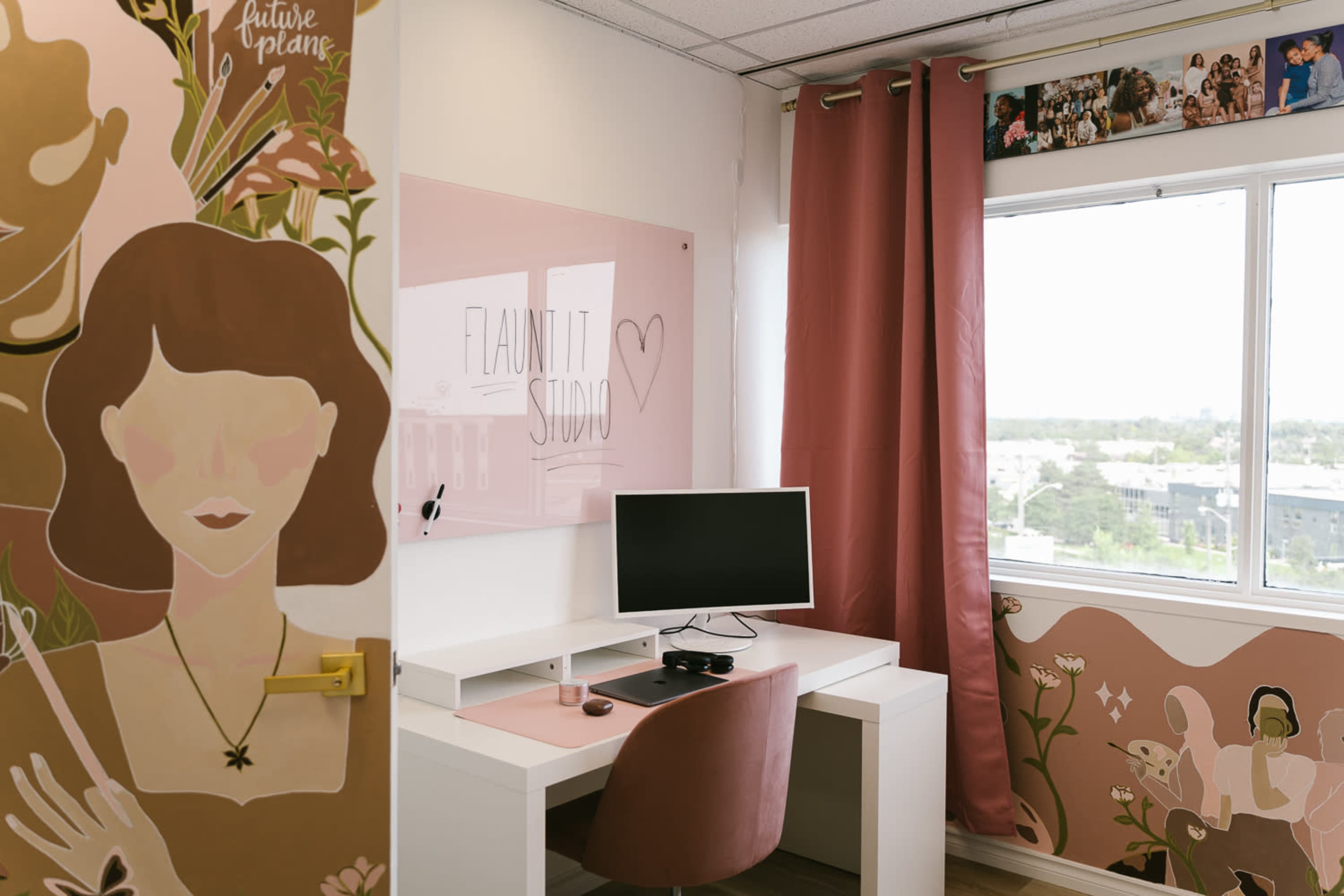 The image shows a brightly lit office space featuring a desk with a computer, pink curtains, and decorative wall art.