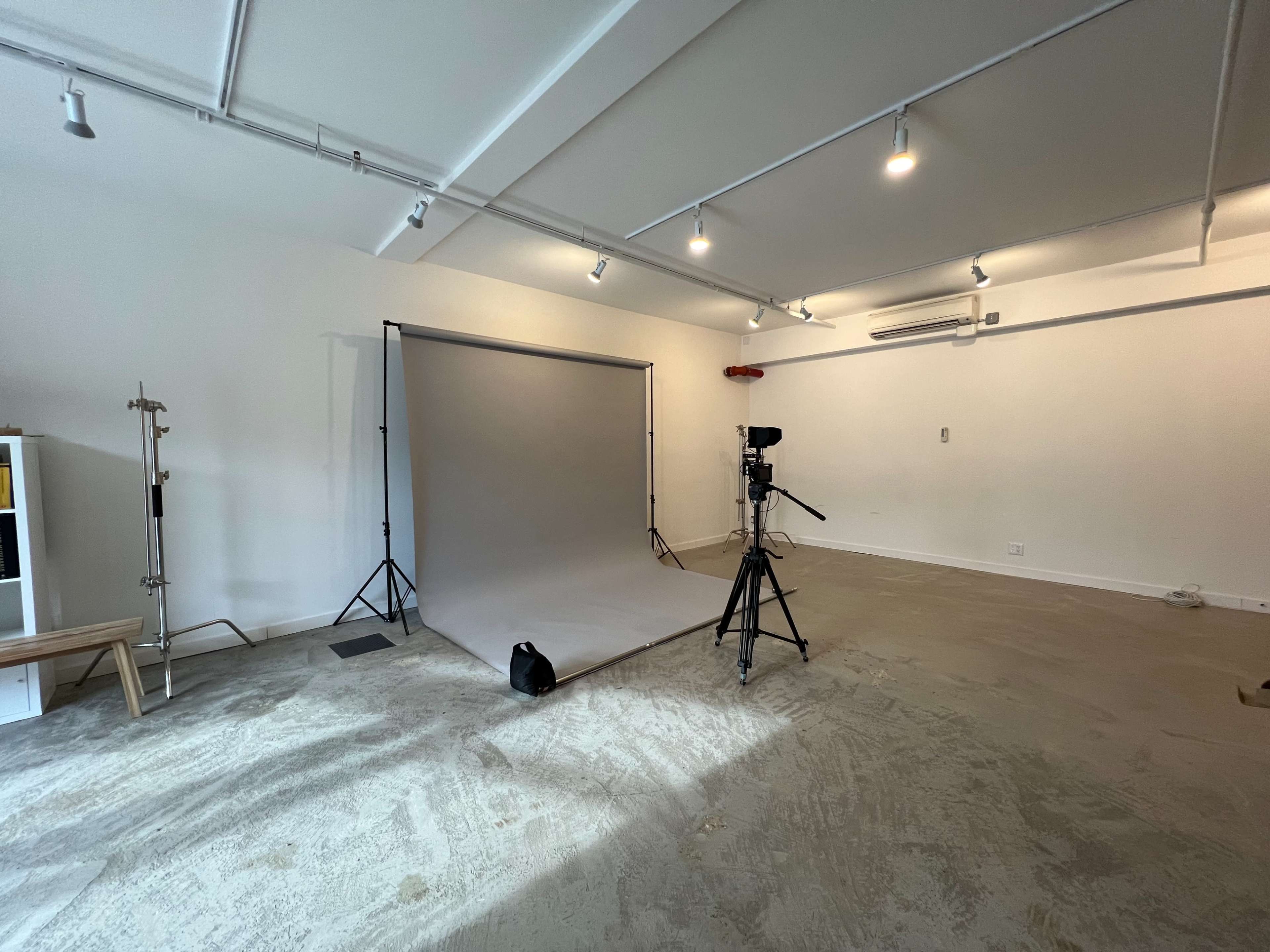 A minimalist studio space with a grey backdrop, a camera on a tripod, and minimal furniture.