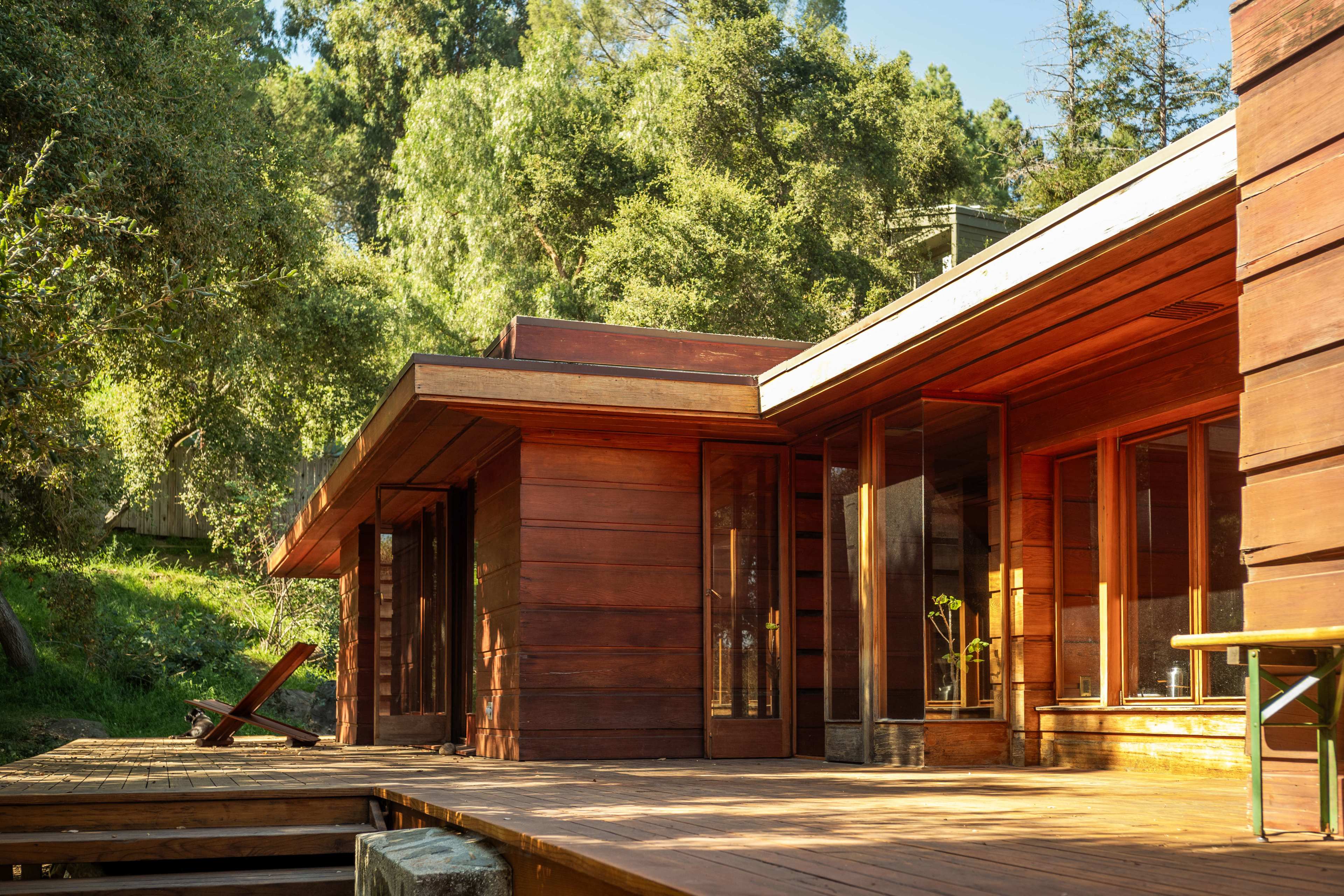 A wooden house with large windows, situated on a deck surrounded by trees.