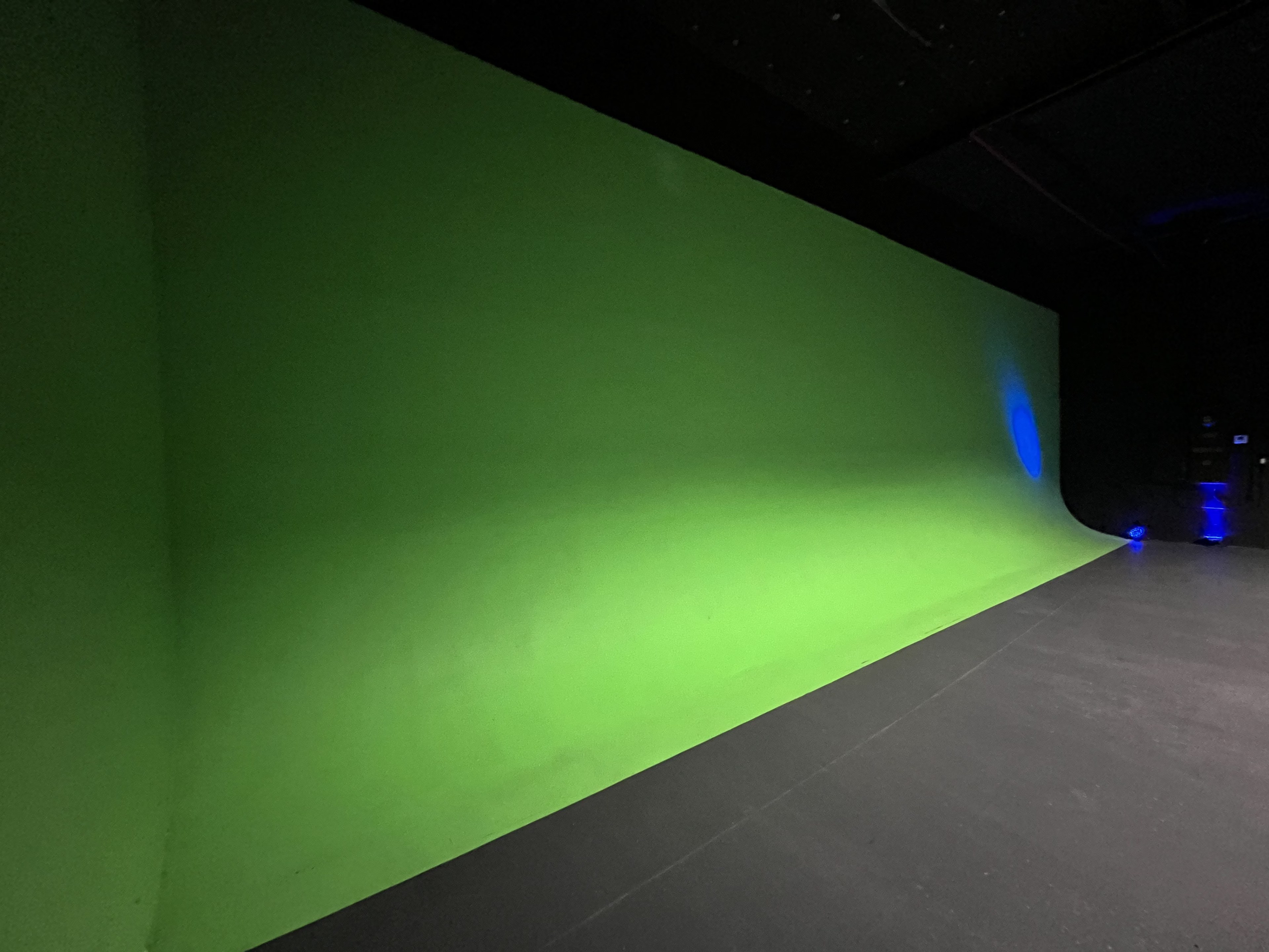 A large green screen in a dimly lit studio.