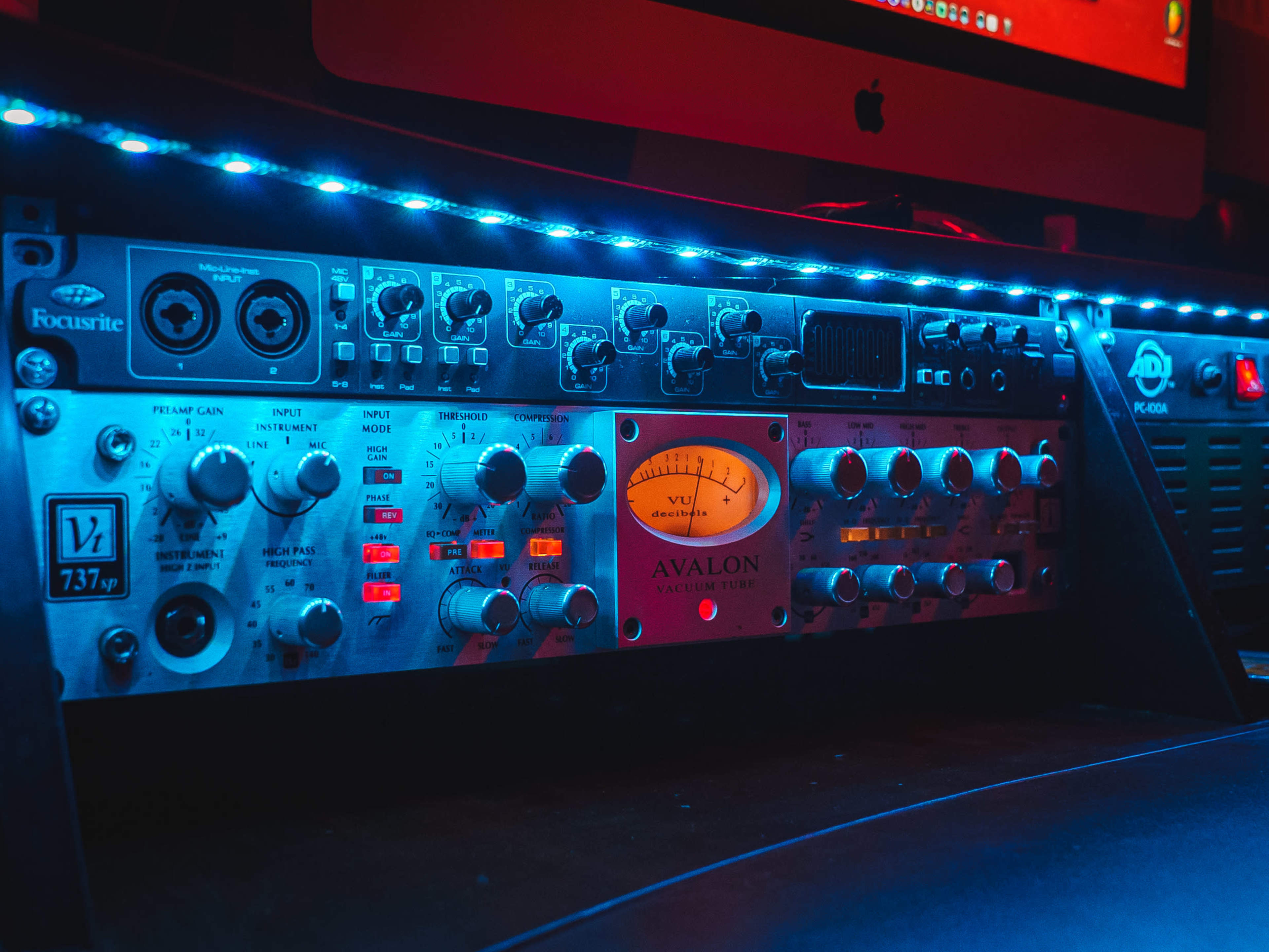 A rack of audio equipment illuminated by blue LED lights, with a prominent Avalon compressor and various controls on display.