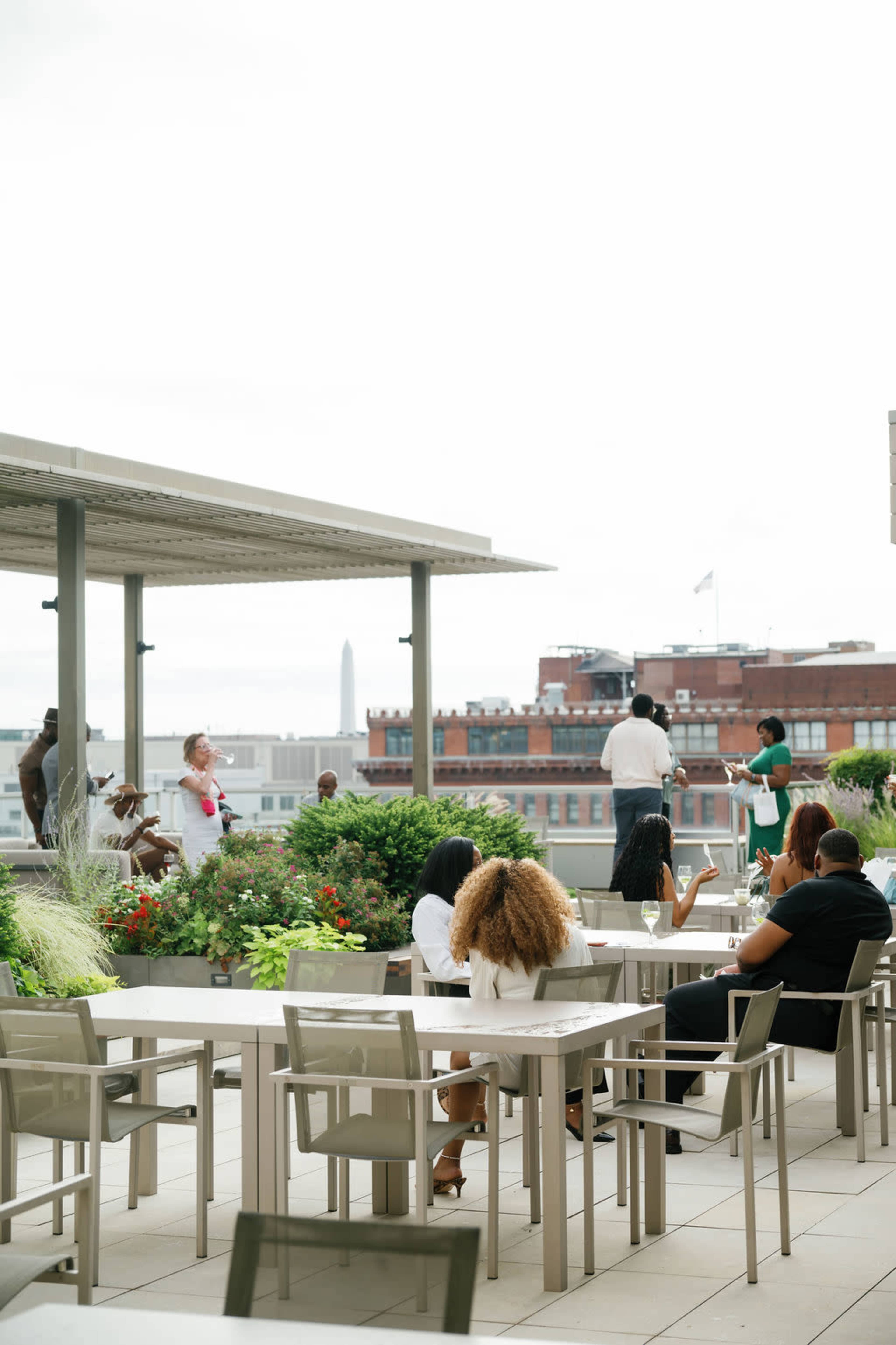 A group of people is gathered on a rooftop terrace, enjoying the view of a cityscape with a monument in the distance.